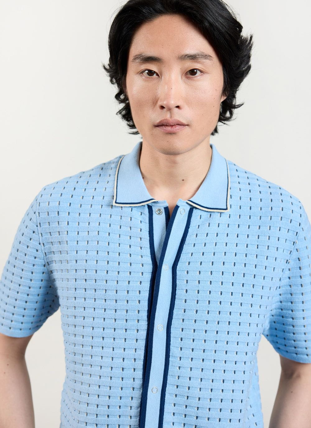 A close-up of a model wearing the Percival Broken Stripe Knitted Shirt in blue, showing the textured knit and popper details.
