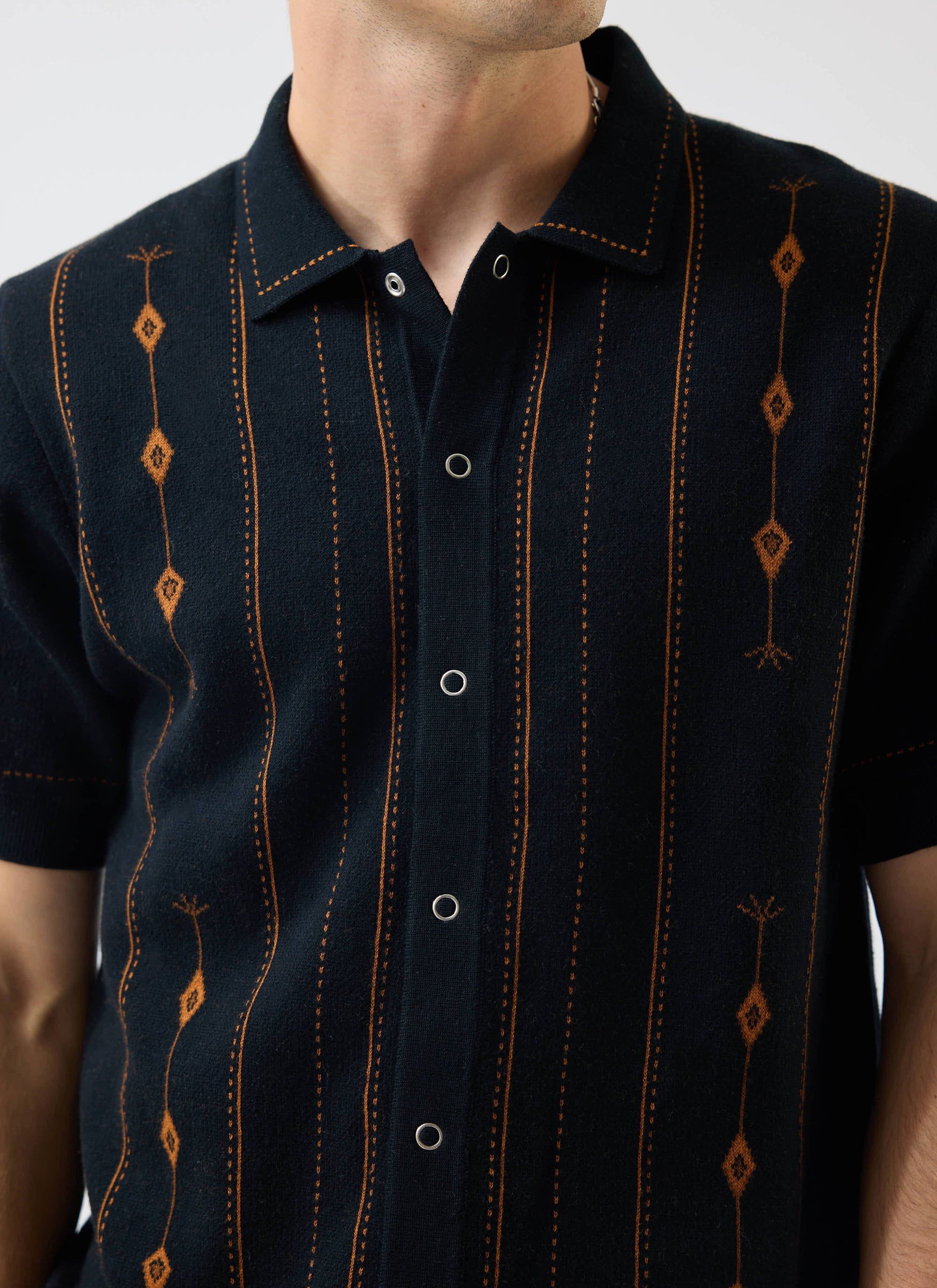 Close-up of the Percival Folio Knitted Shirt in dark navy, showing the book spine jacquard design in tobacco & snap buttons.