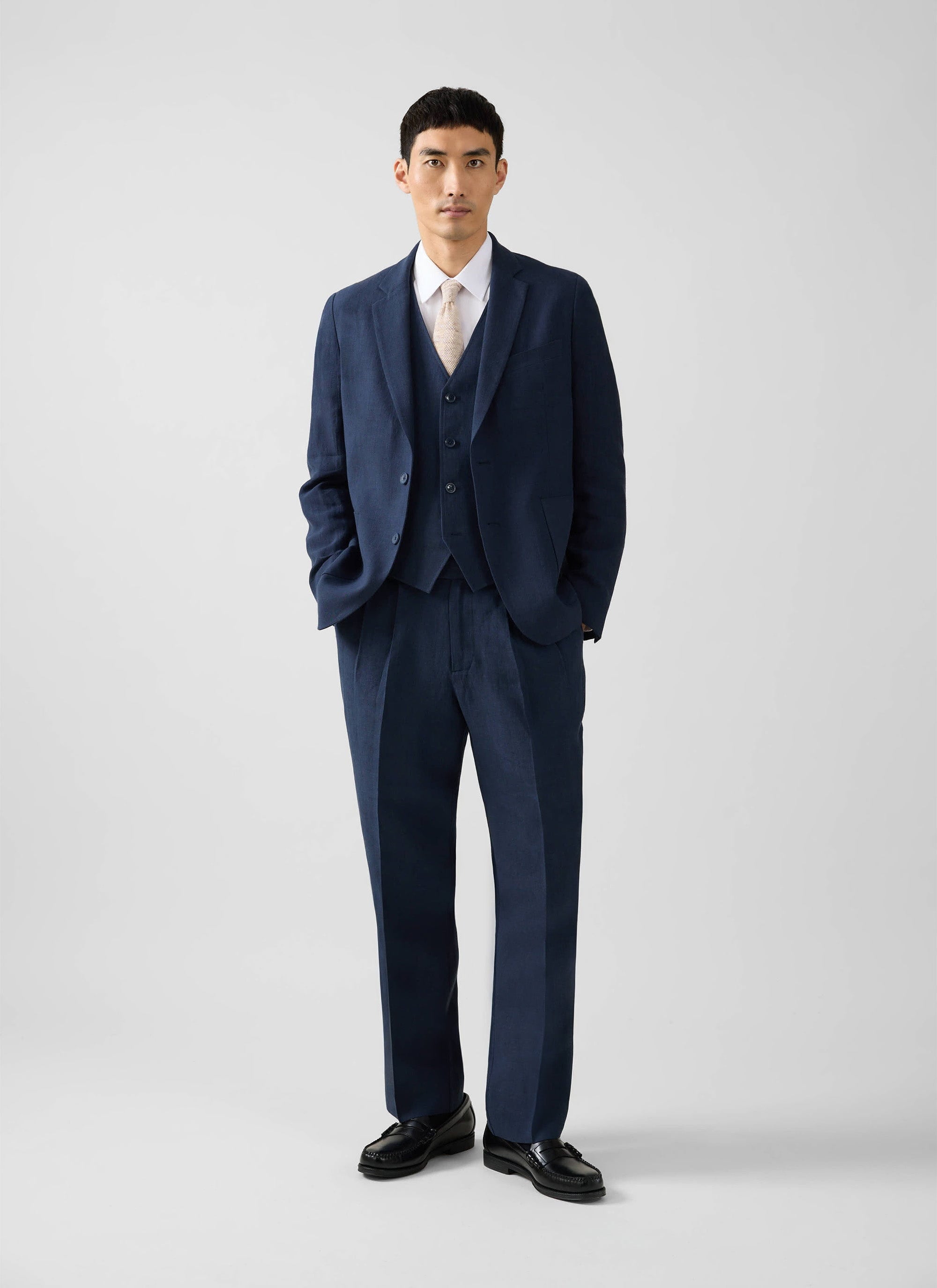 Model wears the Percival Tailored Linen Blazer in navy, styled as a three-piece suit with a white shirt and tie.
