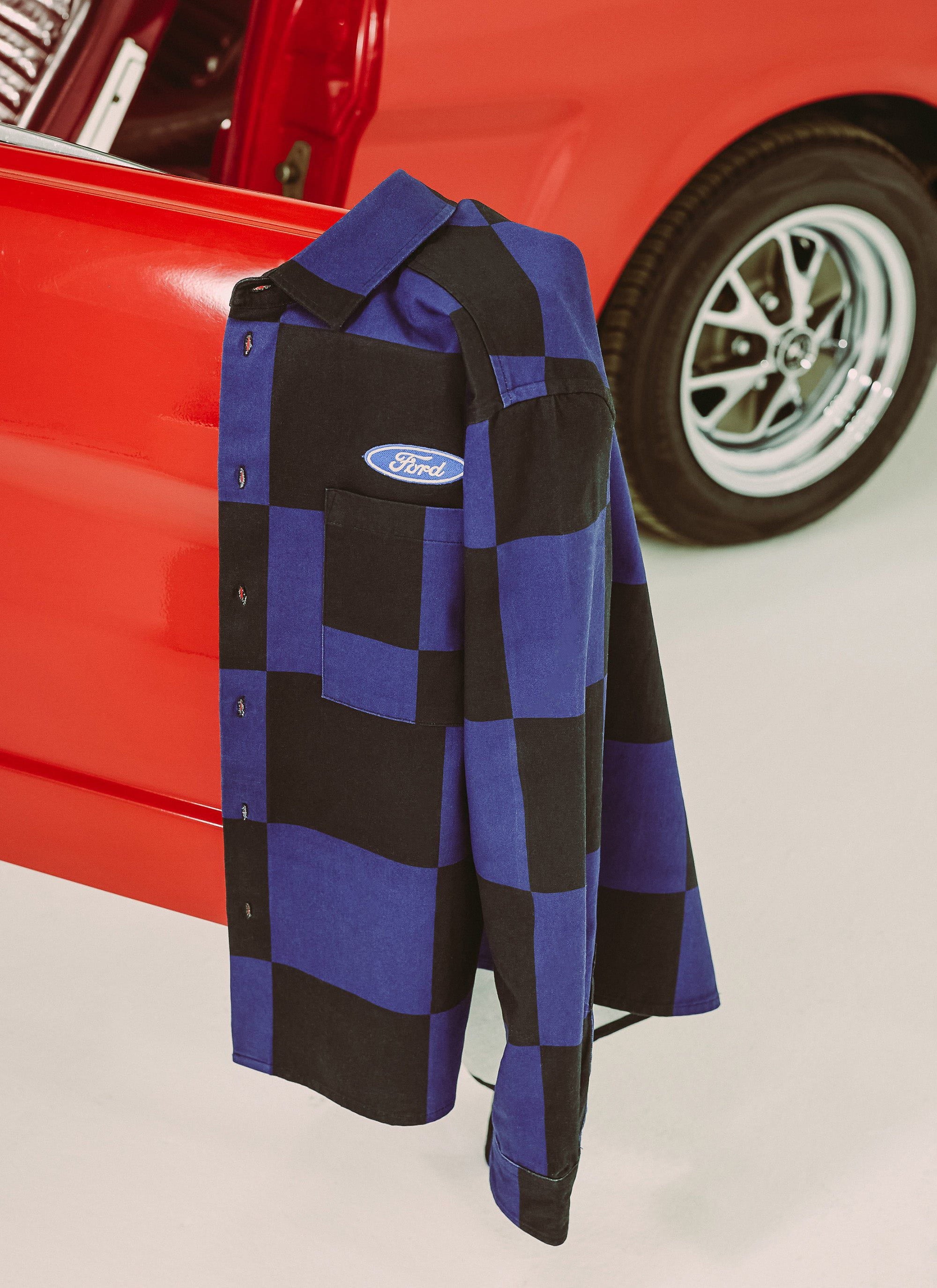 The Percival x Ford collaboration navy and black checkerboard overshirt hanging from a classic red Ford Mustang