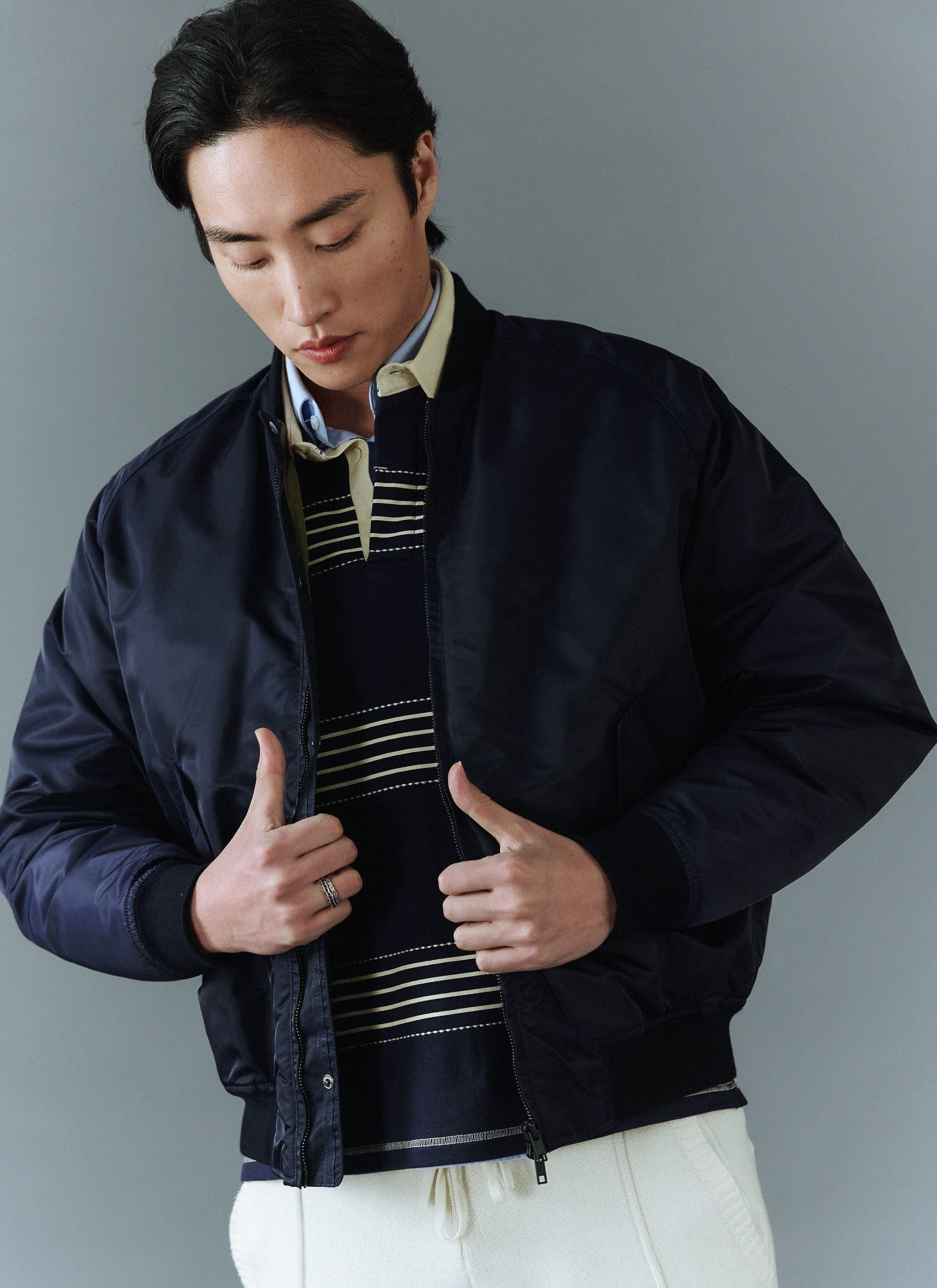 A man wearing the Percival midnight navy bomber jacket, styled open over a striped jumper and collared shirt.