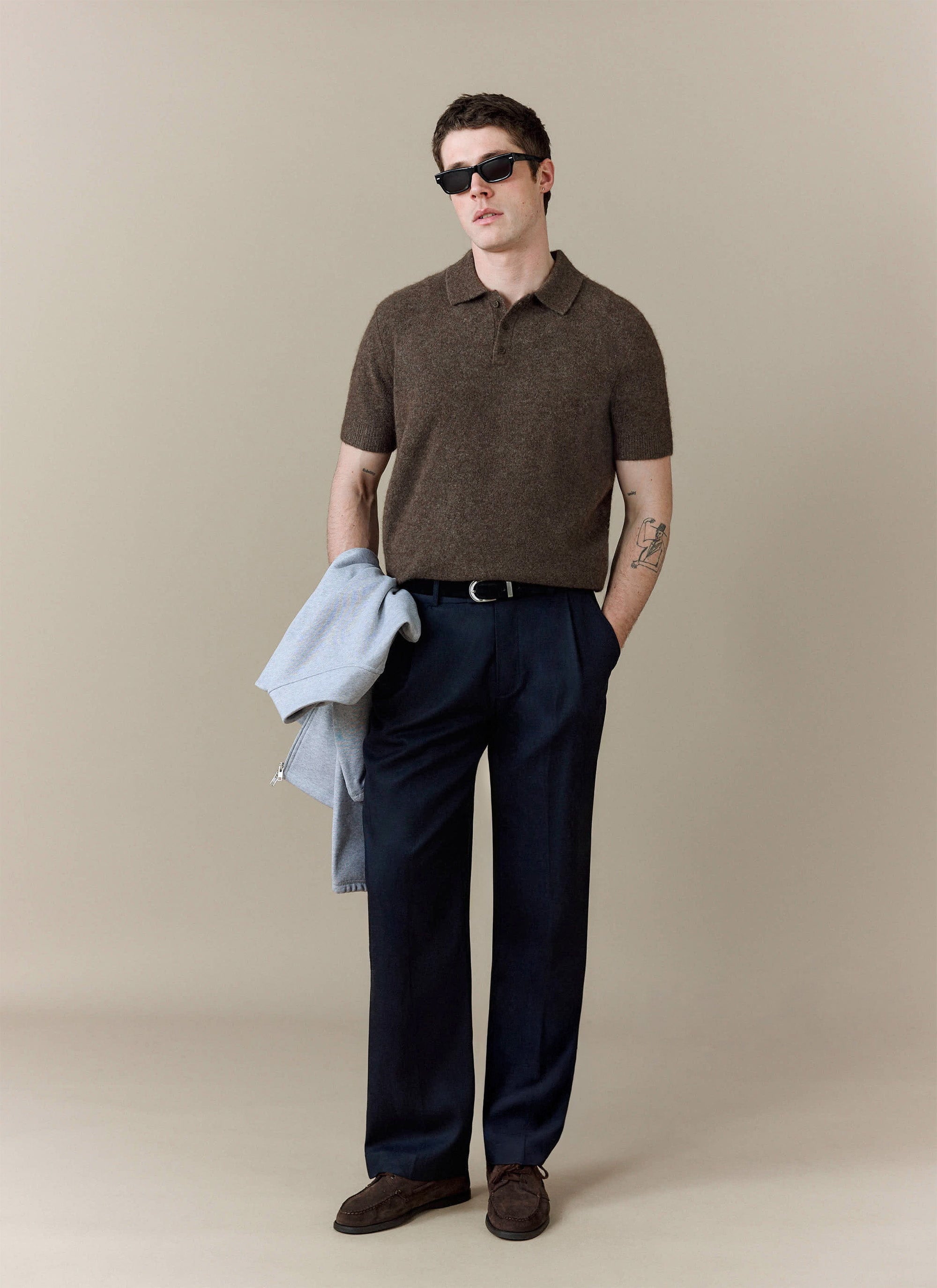 A model wears the Collins Boxy Knitted Polo in Espresso from Percival, styled with dark tailored trousers and sunglasses.