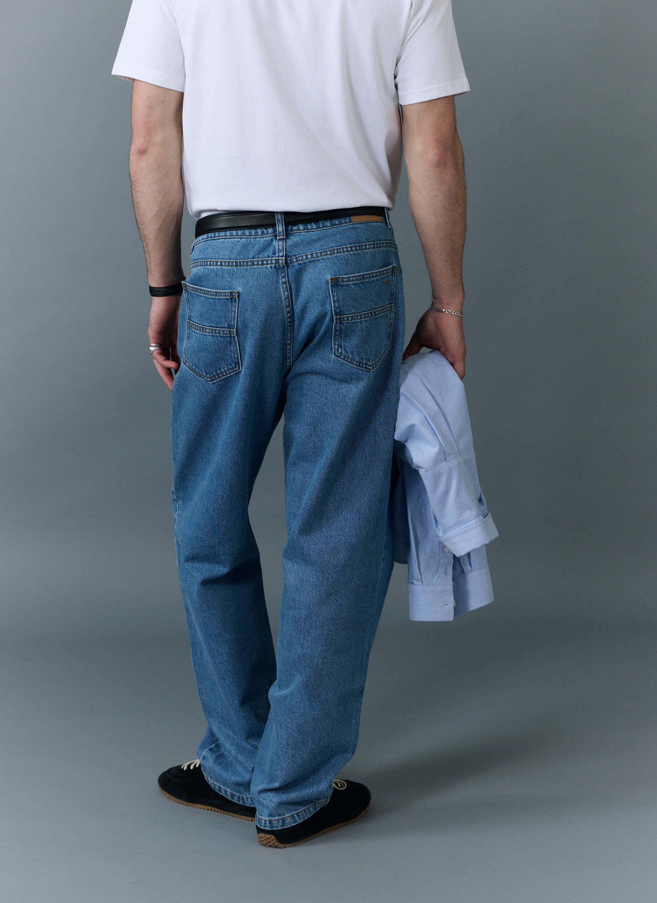 A rear view of a model wearing the Percival Wide Leg Denim Jeans in light wash blue with a white t-shirt.