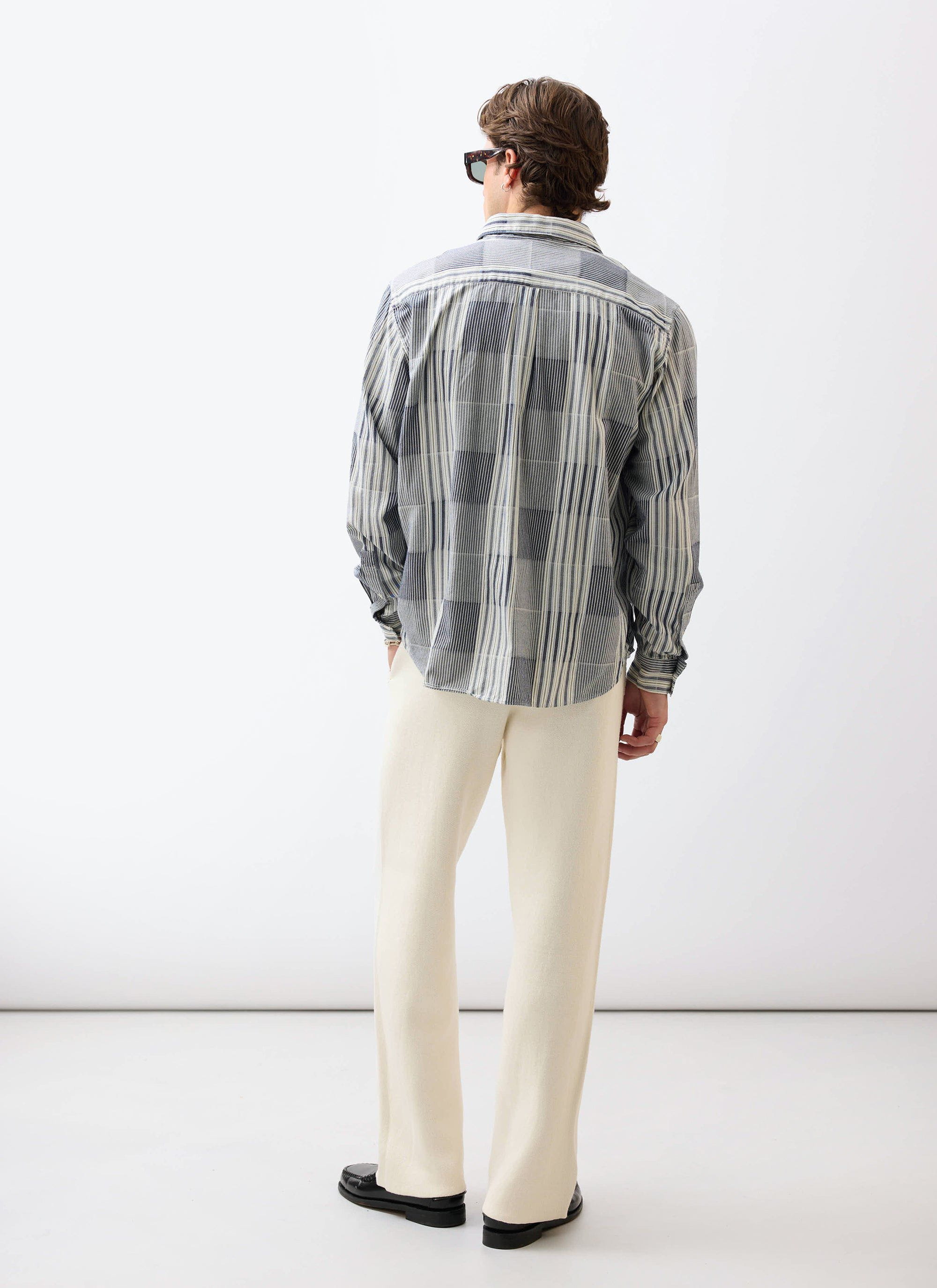 A model seen from the back wearing the Percival Epigraph Patchwork Pearce shirt in blue with cream trousers.