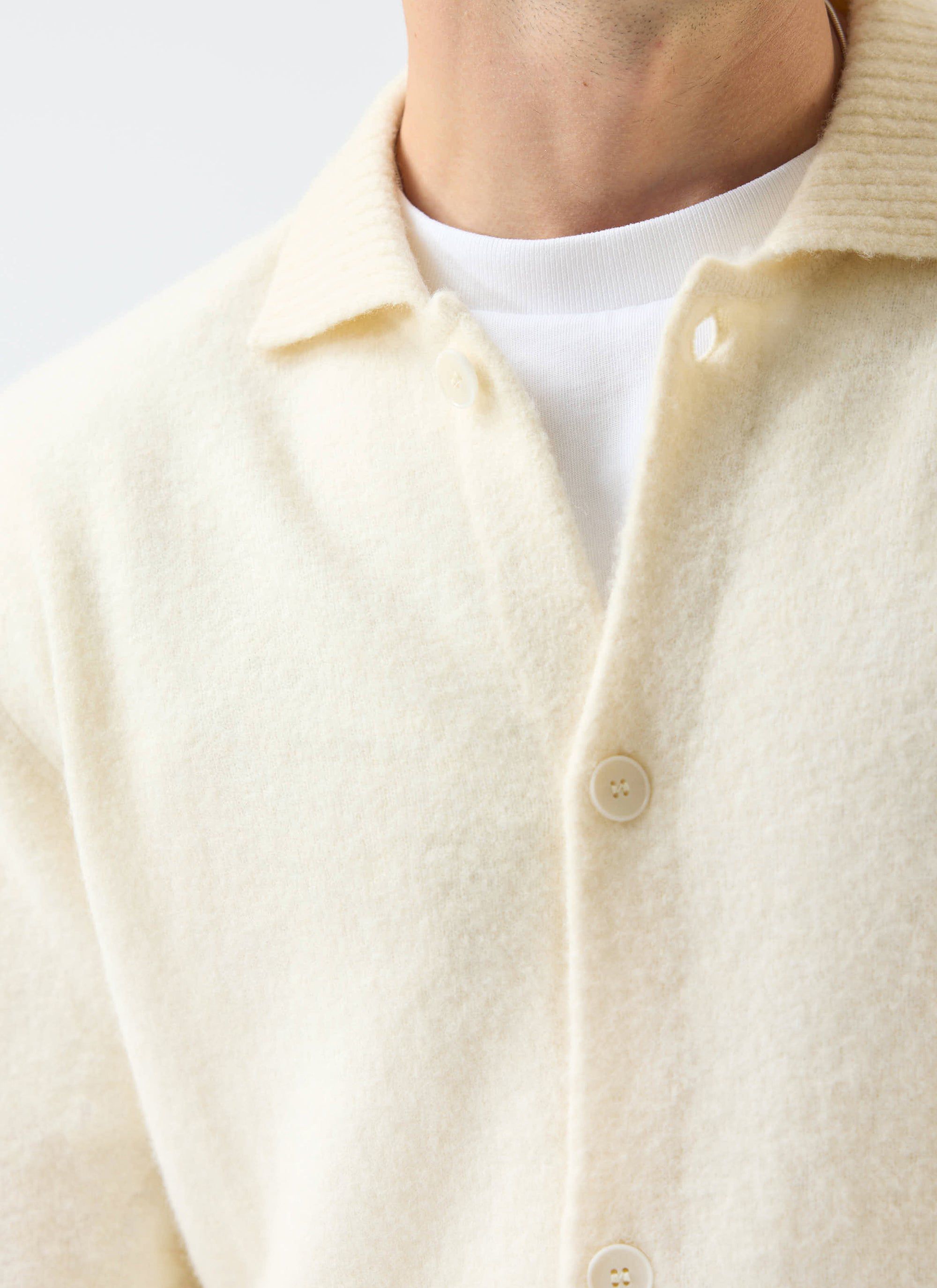 A close-up of a model wearing the Percival Archive Wool Collared Cardigan in ecru cream over a white t-shirt.