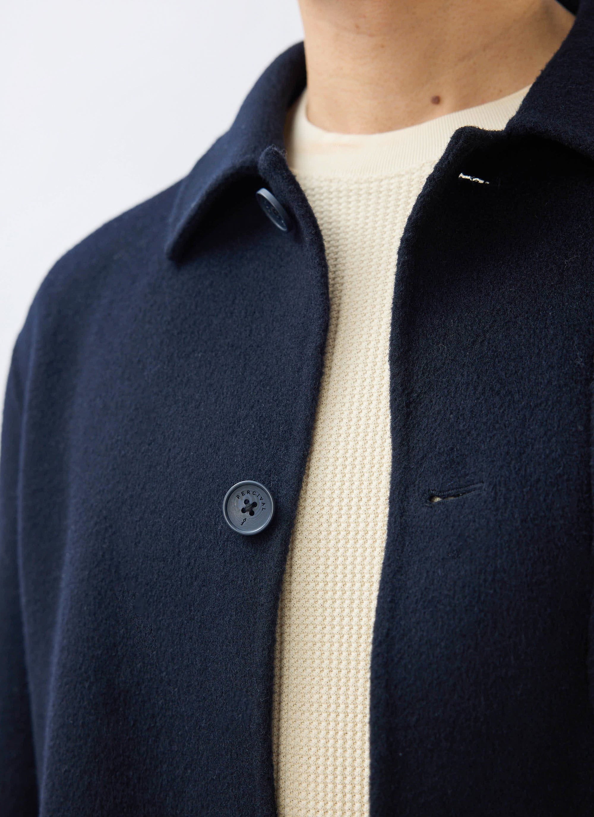 A close-up of the navy Heavy Wool Overshirt from Percival, showing the textured fabric and a branded button.