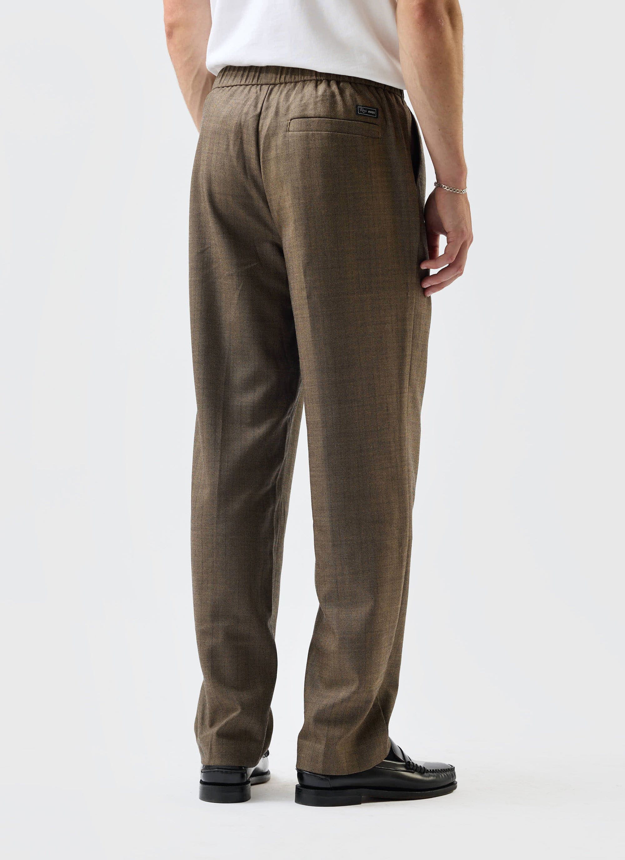 A model seen from behind wearing the Percival Grounds Relaxed Trousers in Oak herringbone wool, styled with loafers.