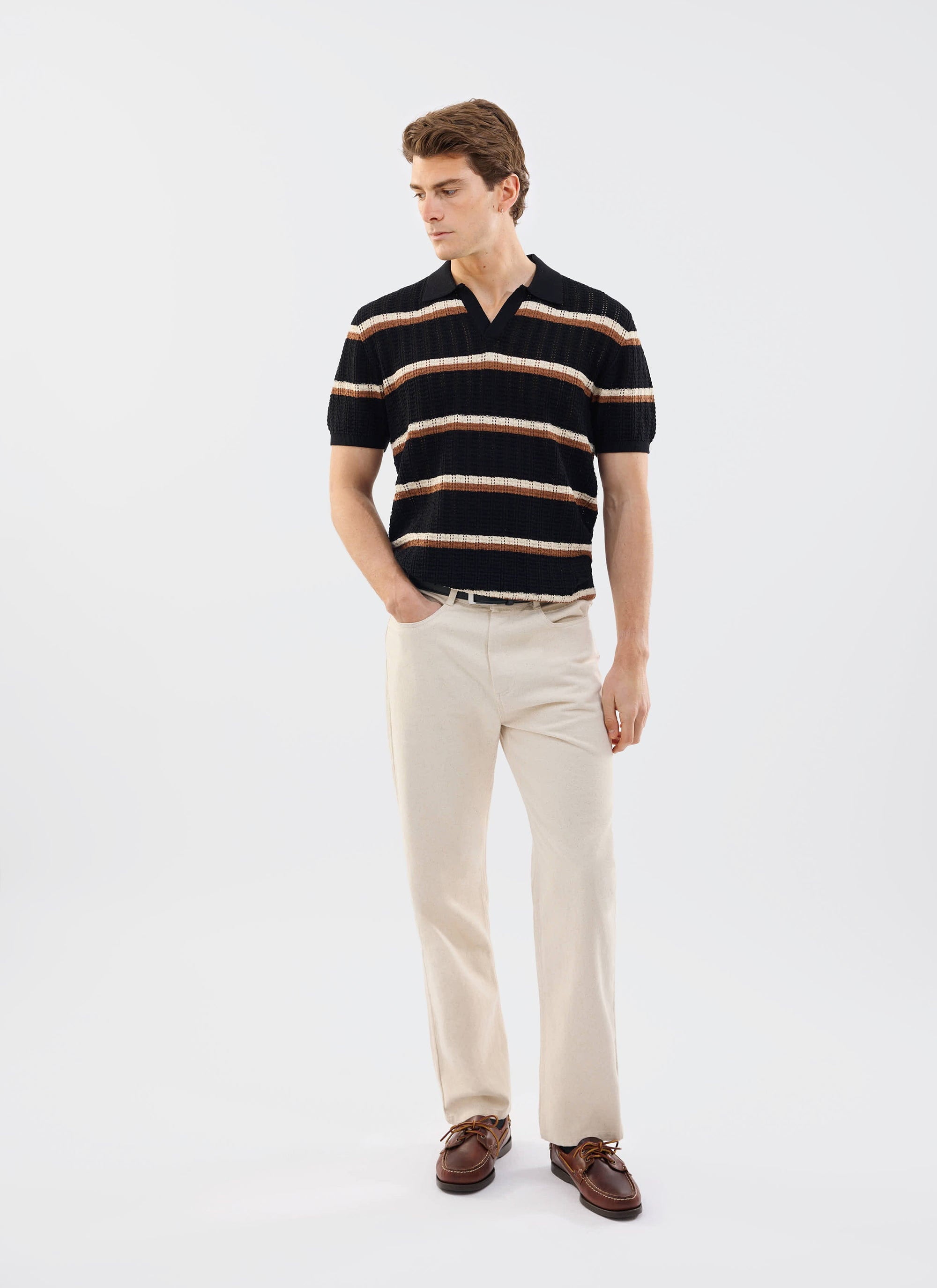 A model wears the Percival Tessaro Knitted Stripe Polo in black, styled with cream trousers against a white background.