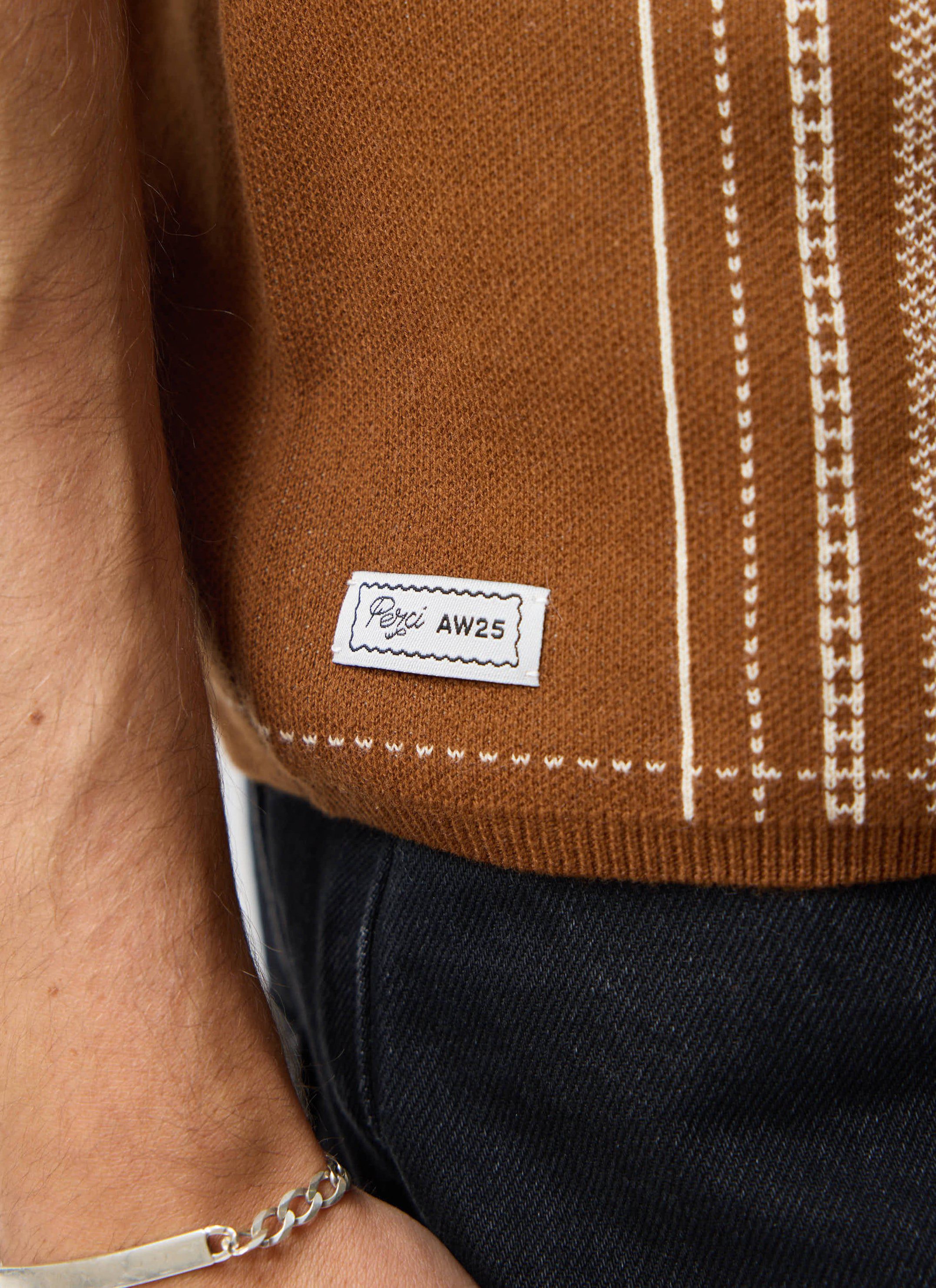 A close-up of the jacquard pattern and brand label on the hem of the Percival Accolades Knitted Shirt in tobacco brown.