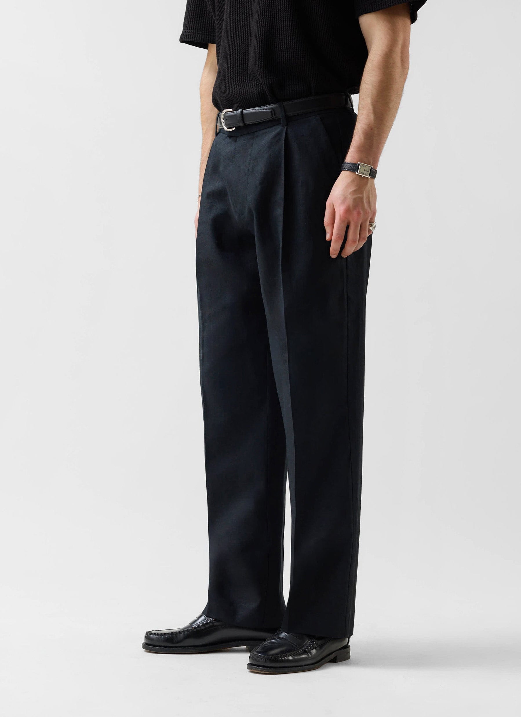 A studio shot of a model wearing the Percival Wide Leg Linen Trousers in black, styled with a black knit top and loafers.