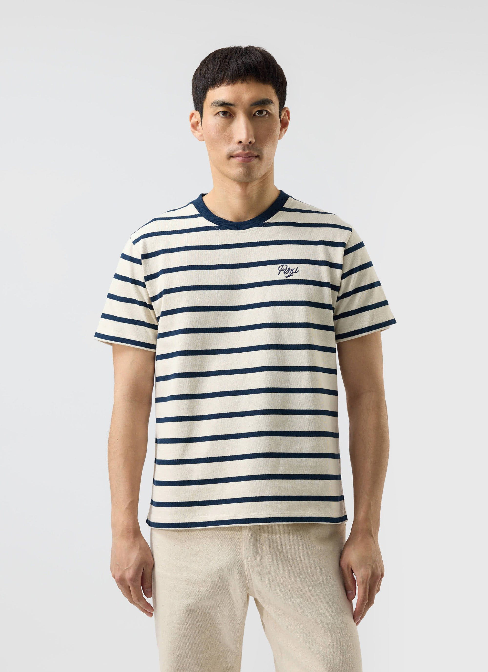 A man models the Percival Breton Stripe T-shirt in ecru and navy against a plain white studio background.