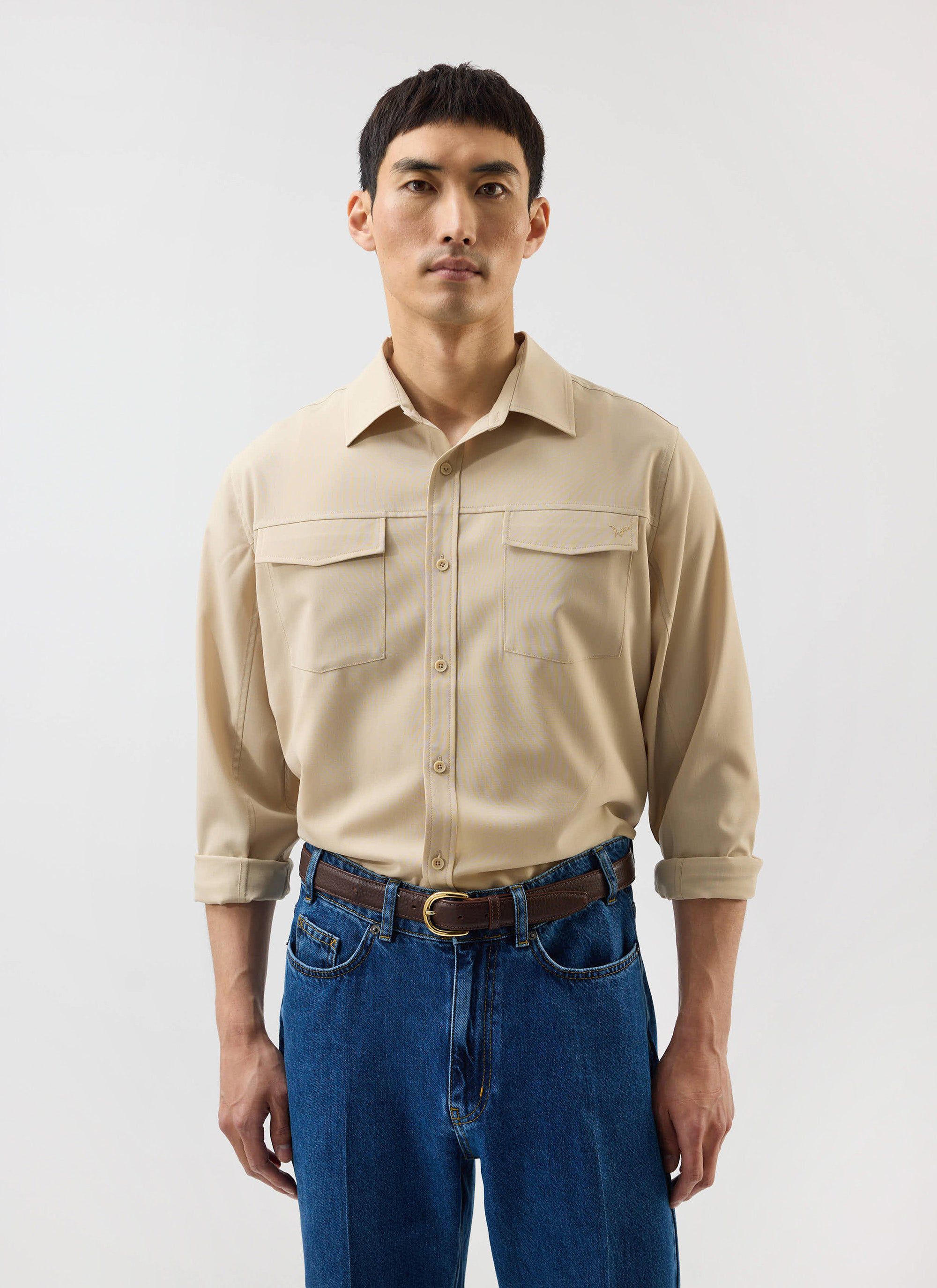 A model wears the camel beige Safari Shirt from the Percival x Warren collection, styled with classic blue jeans.