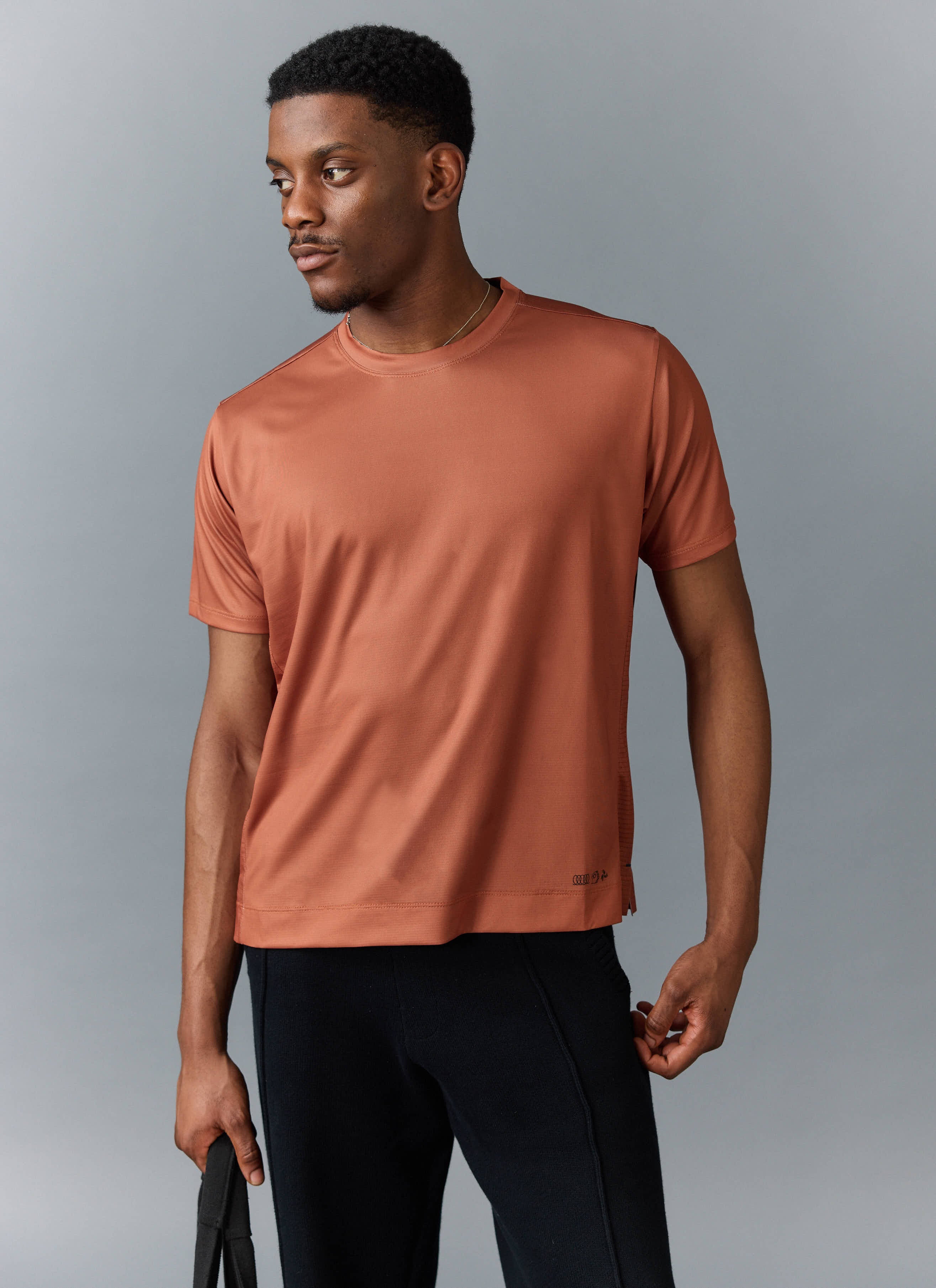 A model wears the Percival PCVL Performance Top in rust, styled with black trousers against a studio background.
