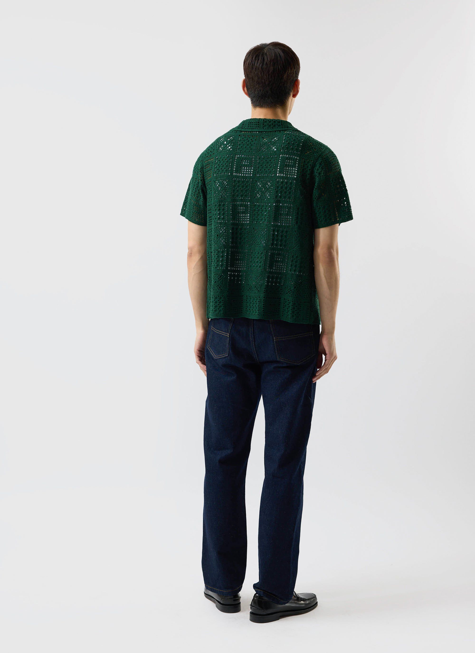 A rear view of a model wearing the Percival Crochet Groundsman Shirt in forest green with dark wash jeans.