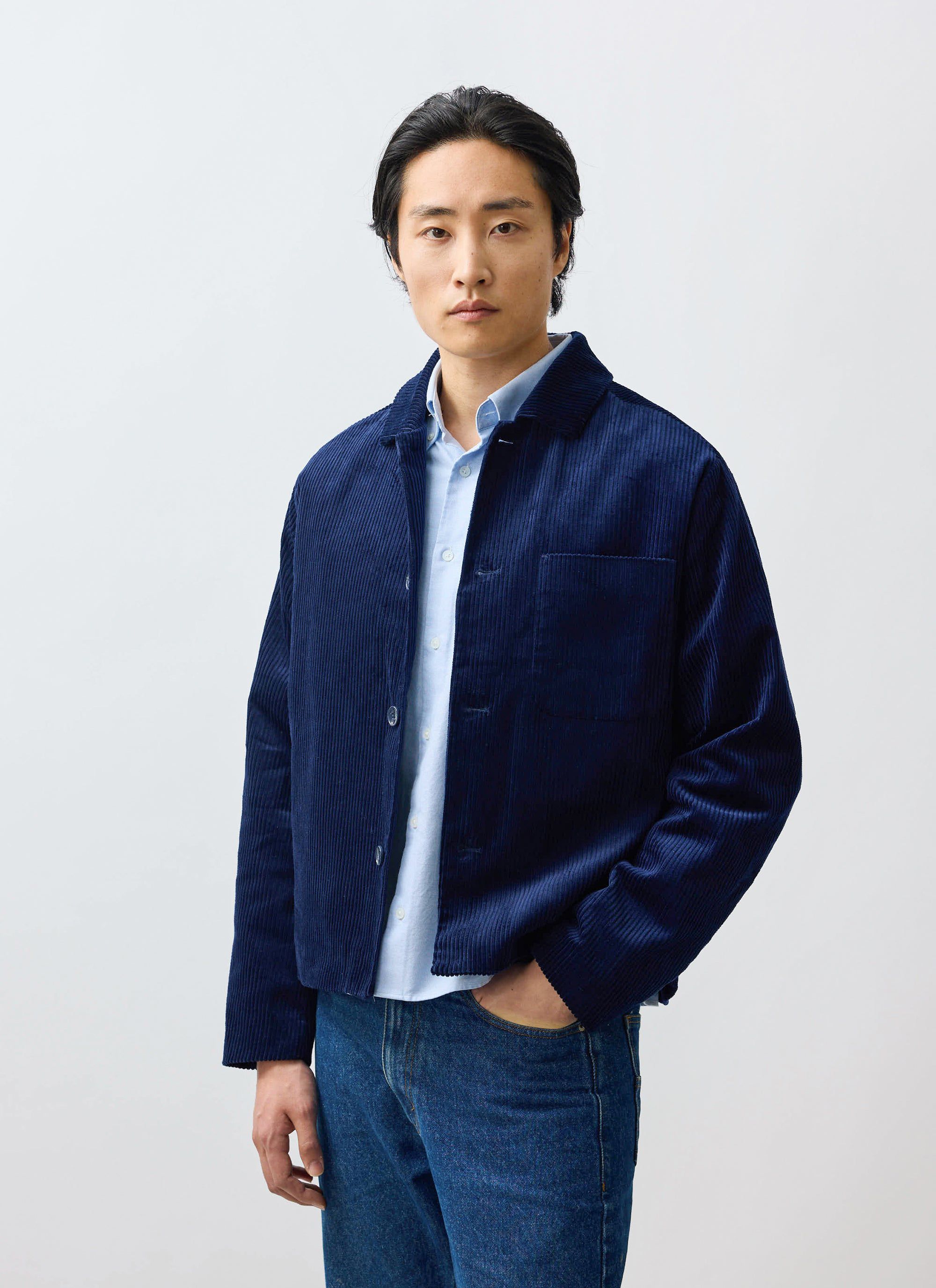 A model wears the Percival Cord Overshirt in navy, layered over a light blue shirt and styled with denim jeans.
