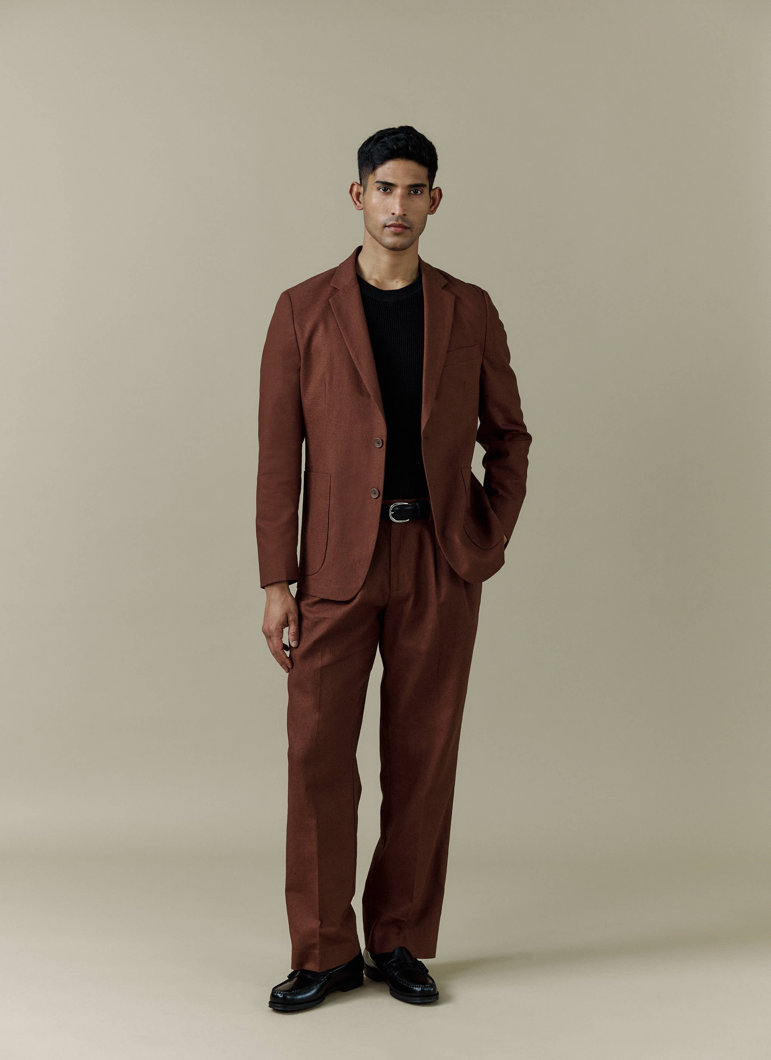A model wears the Percival Tailored Linen Blazer and matching trousers in brown, styled with a black jumper and loafers.