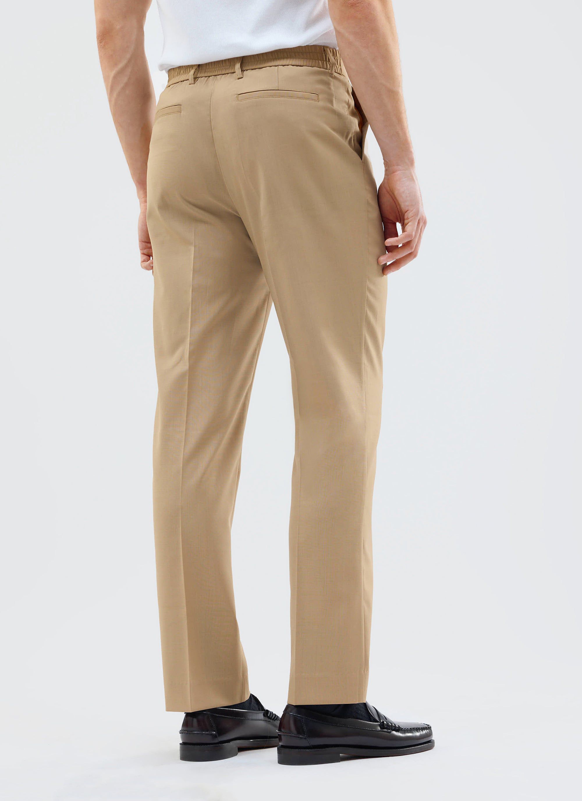 A model shows the back fit of the Percival Tailored Elasticated Waist Trousers in tan, styled with black loafers.