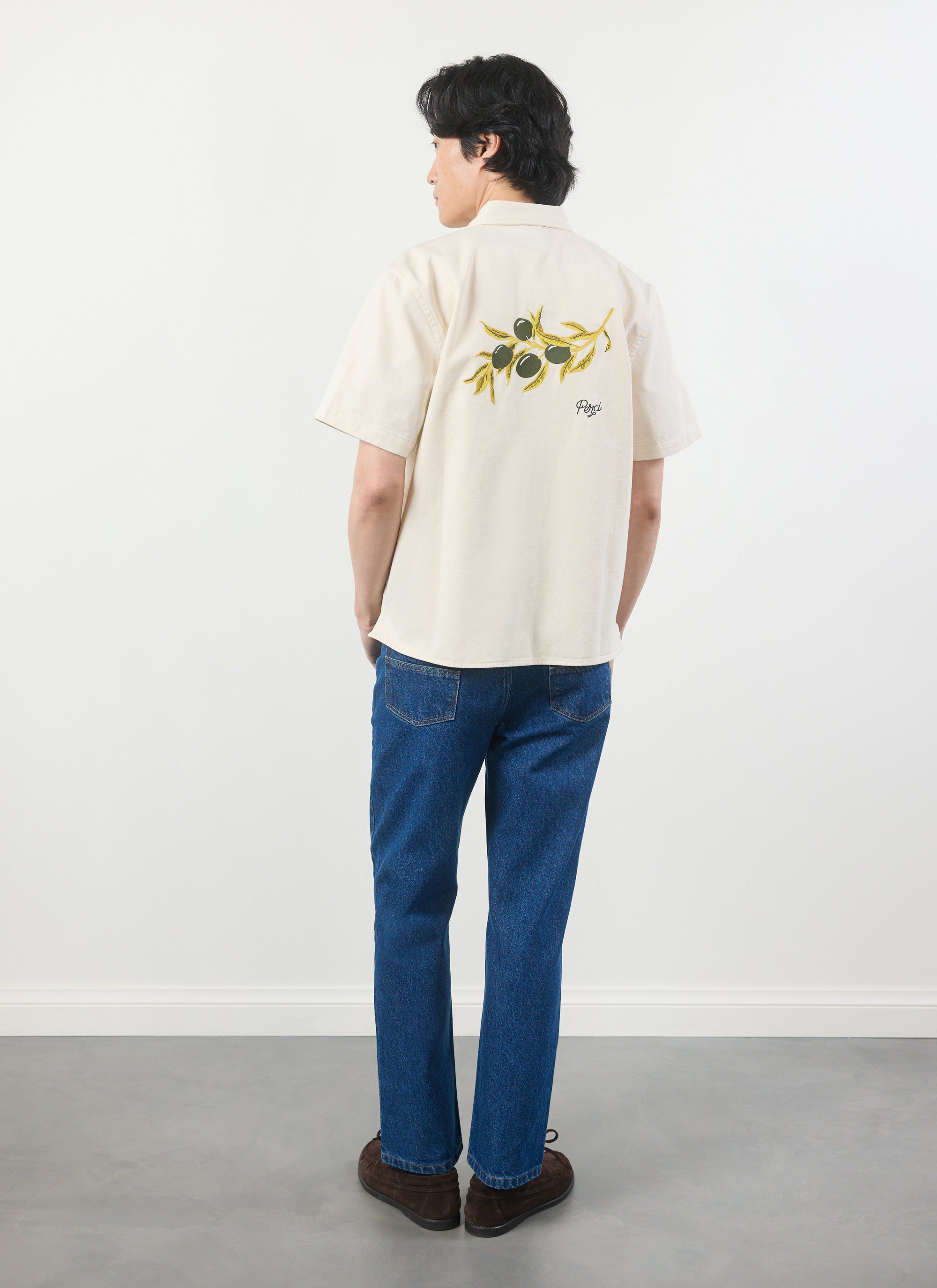 A man models the Percival Olive Embroidered Cropped Shirt in white, viewed from behind to display the olive branch graphic.