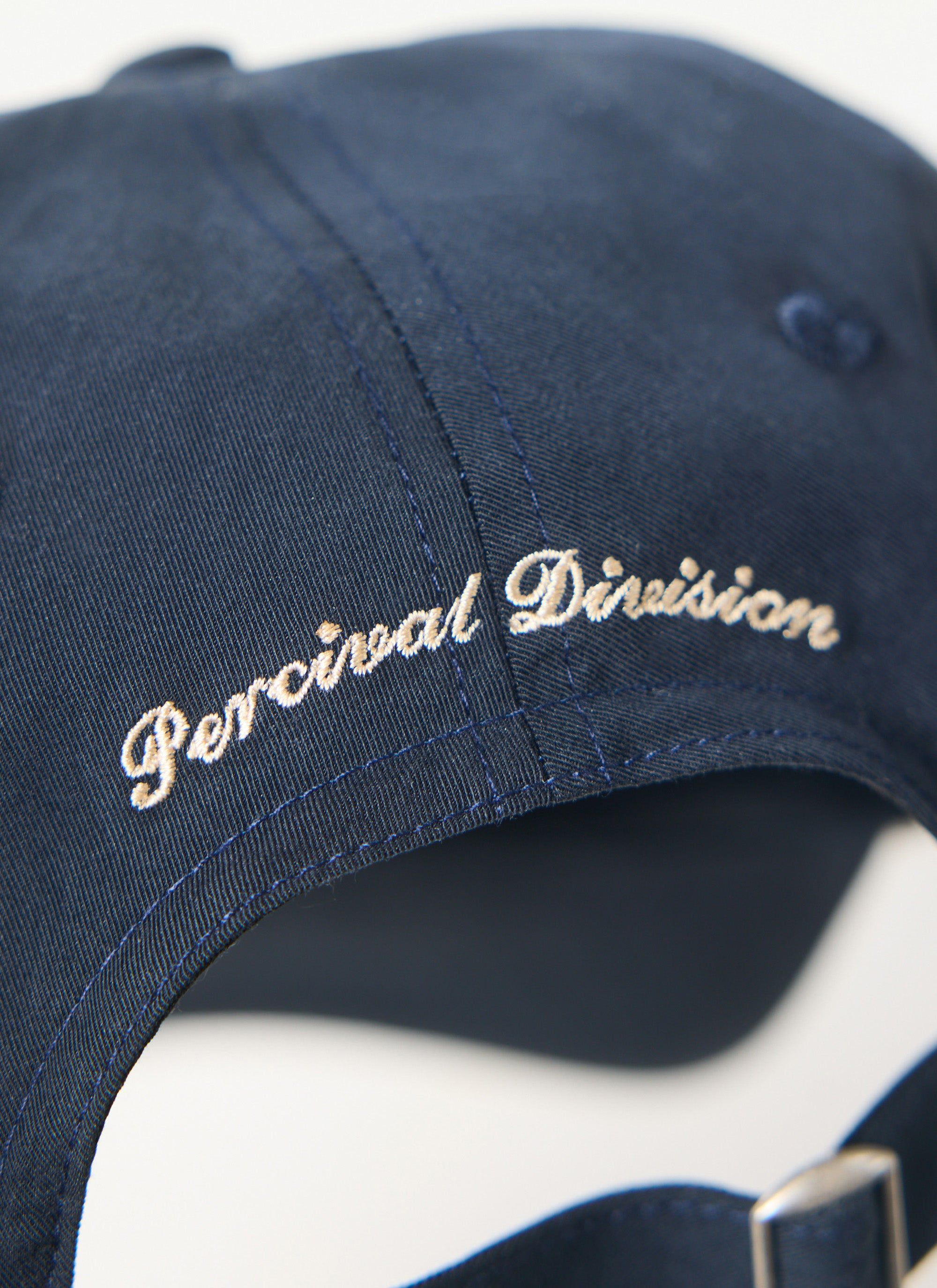 Close up of the navy Percival trucker cap showing the 'Percival Division' ecru embroidery on the back.