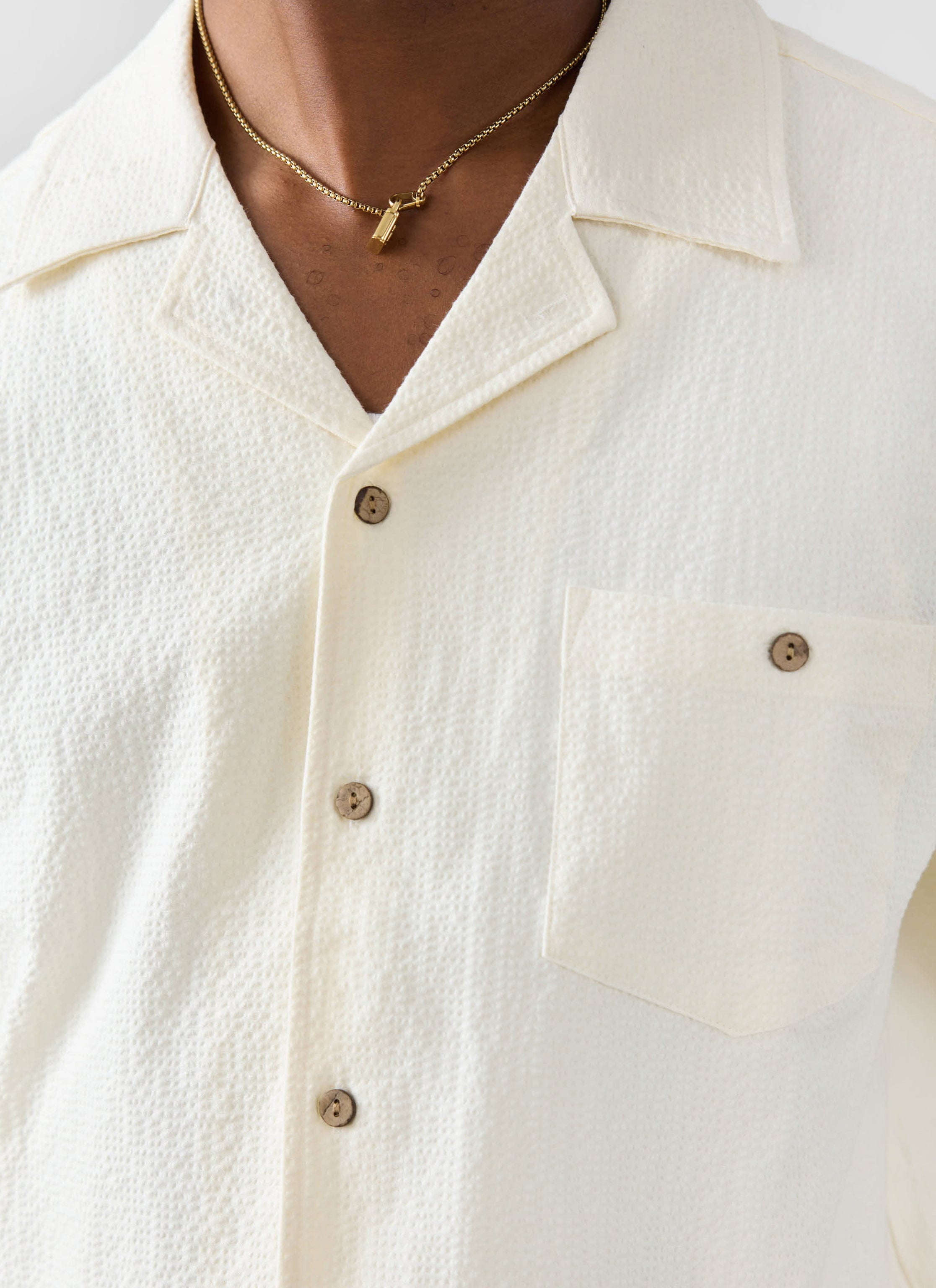 Close up of the Percival ecru seersucker cuban shirt, showing the textured fabric, collar and chest pocket detail.