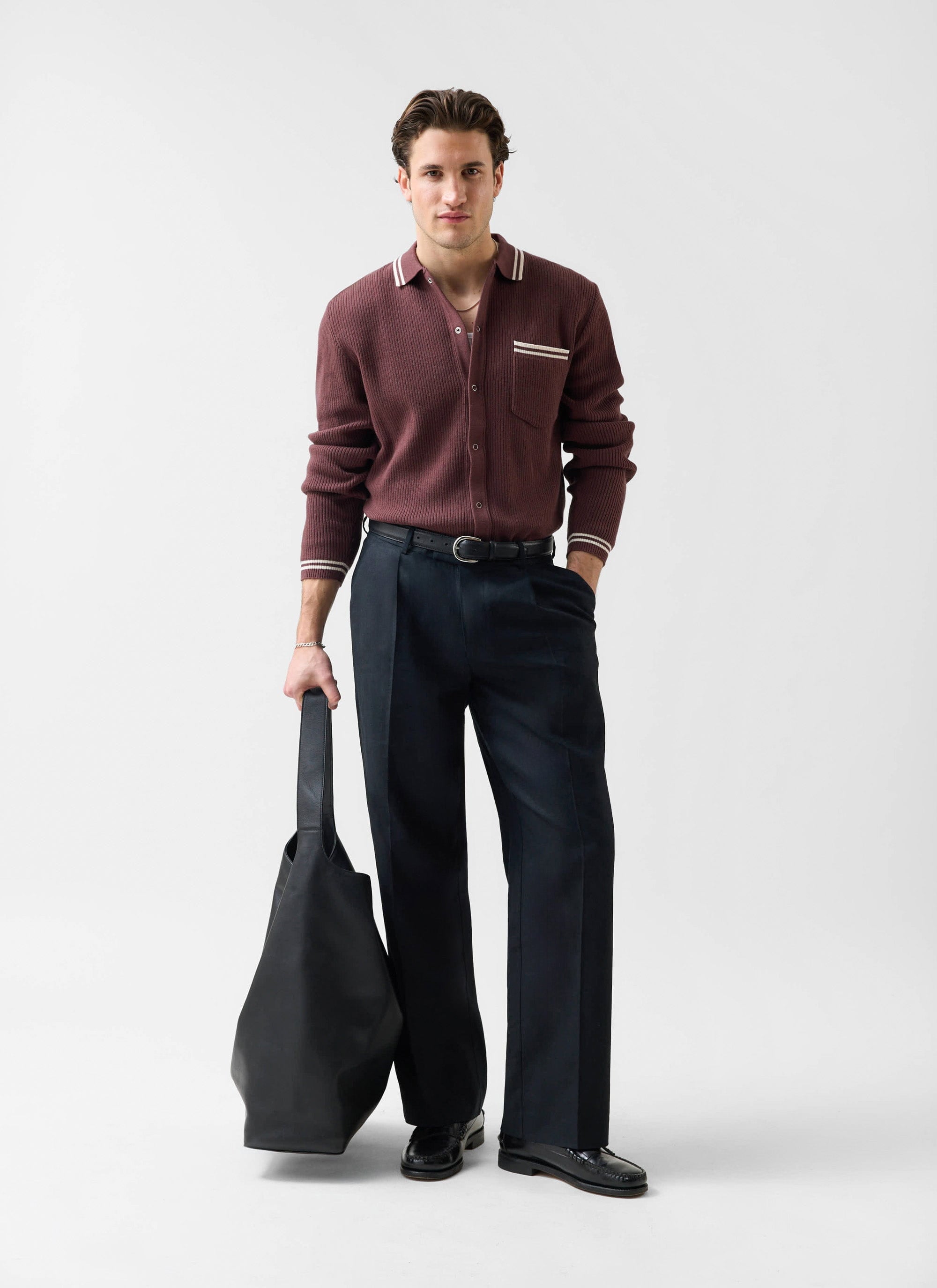 A model wears the Percival Pablo long sleeve knitted cotton shirt in espresso with black trousers and a black bag.
