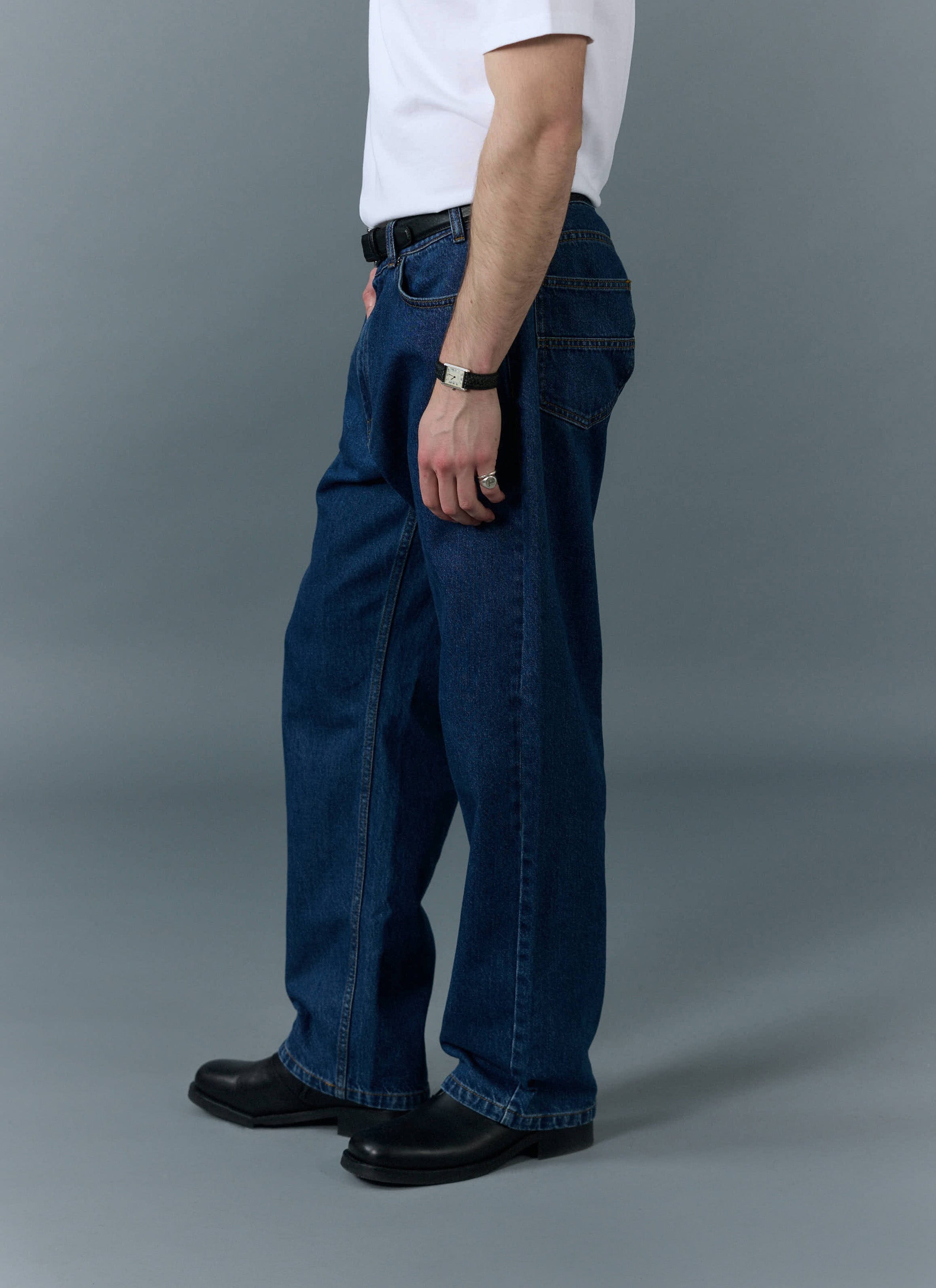 A side profile of a model wearing the Percival Wide Leg Denim Jeans in mid wash blue, showcasing their relaxed fit.