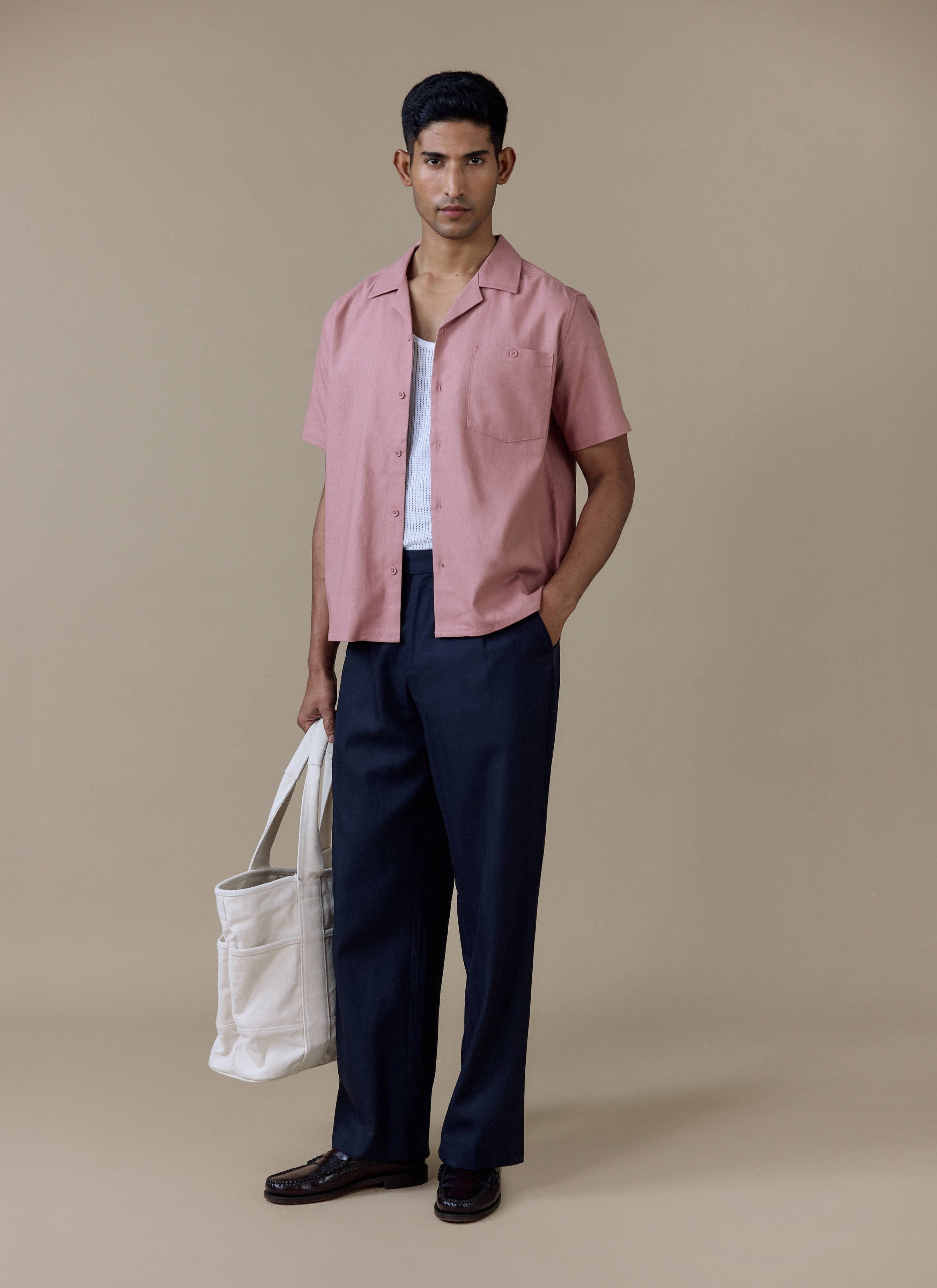 Percival Short Sleeve Cuban Shirt in dusty pink linen, worn with navy pleated trousers and a white canvas tote bag.