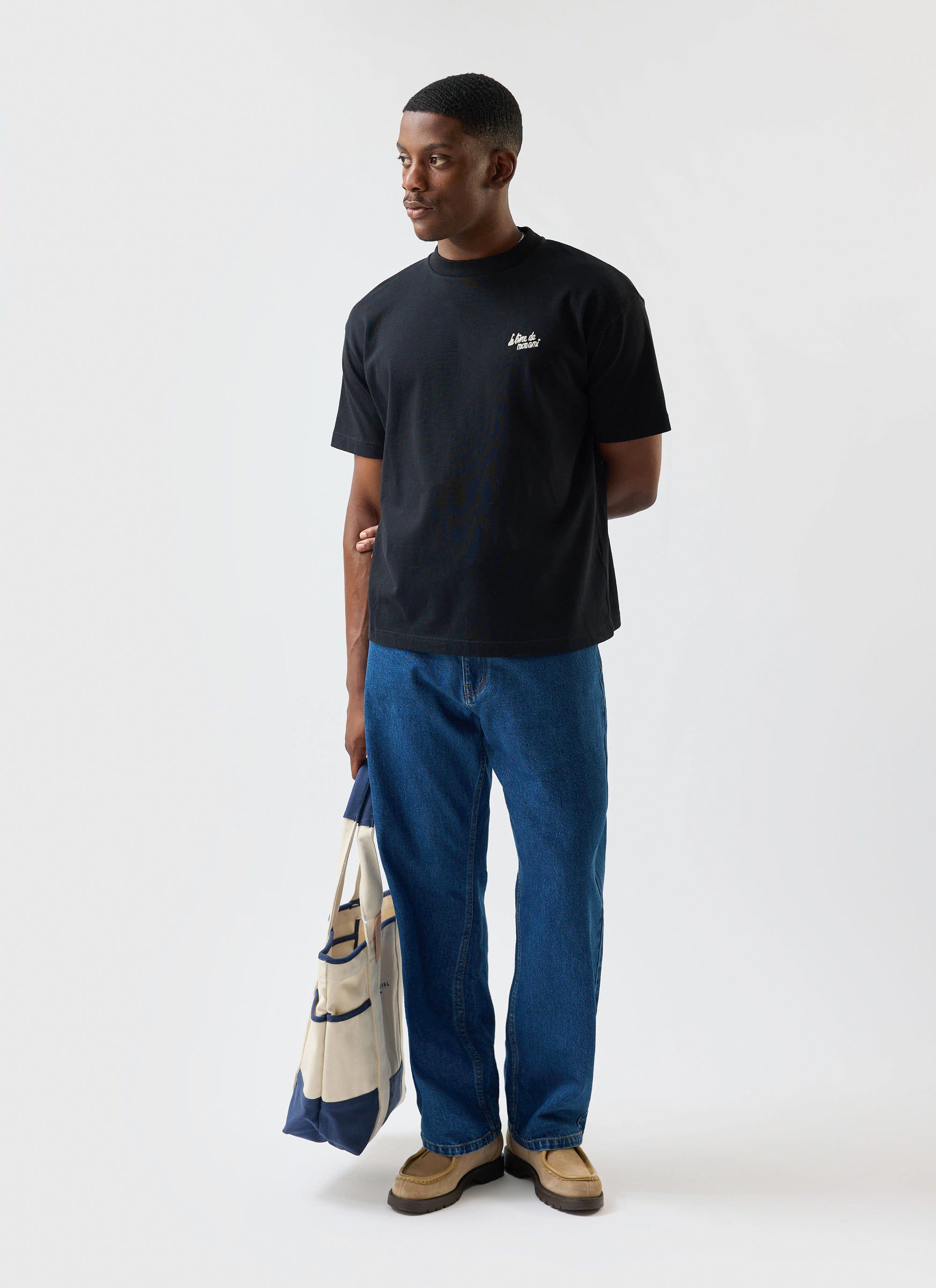 A model wears the Percival Le Livre De Mon Ami oversized t-shirt in black, styled with blue jeans and a tote bag.