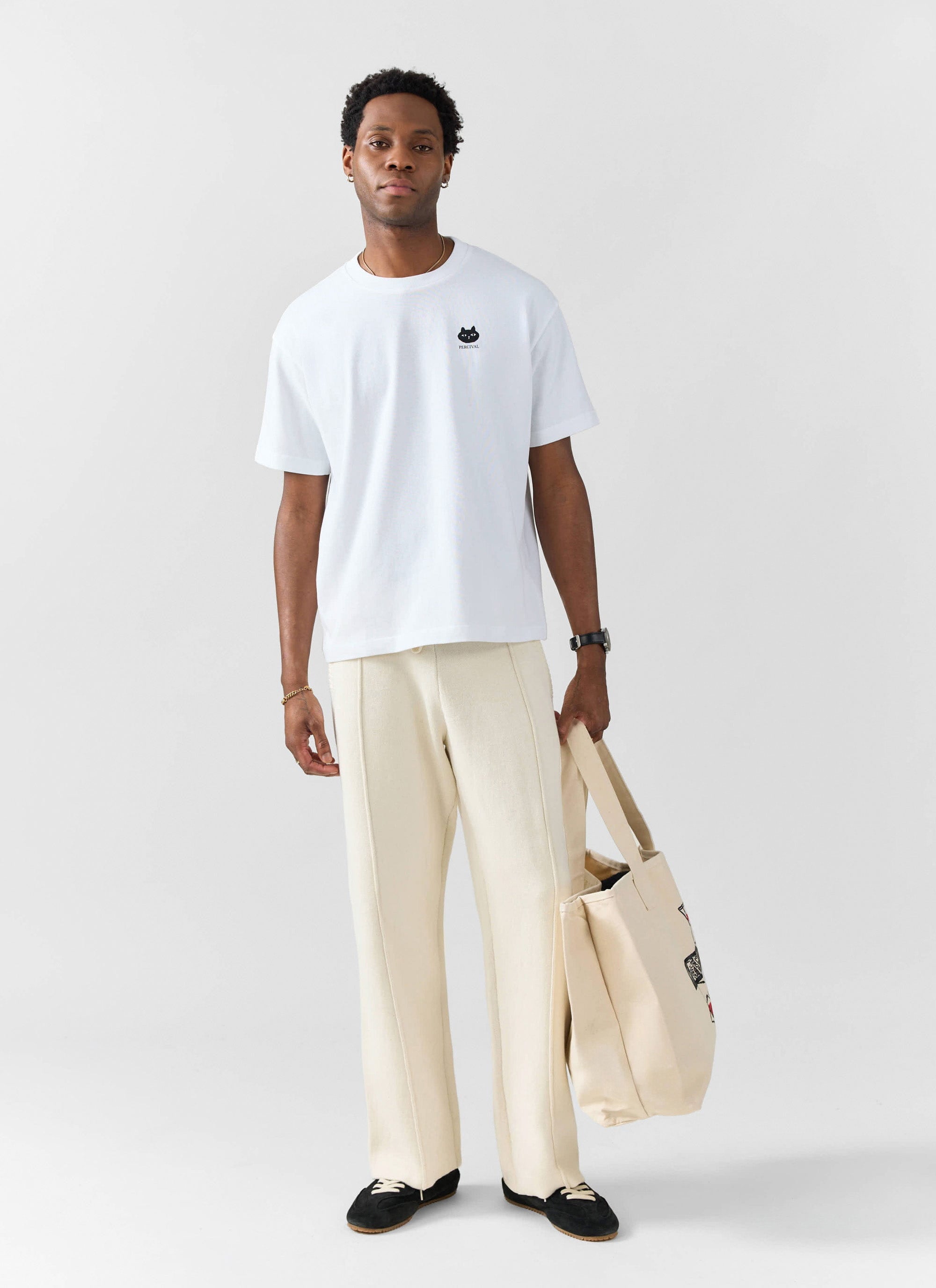 A model wears the Percival Perci Loaf oversized t-shirt in white, styled with cream trousers and holding a tote bag.