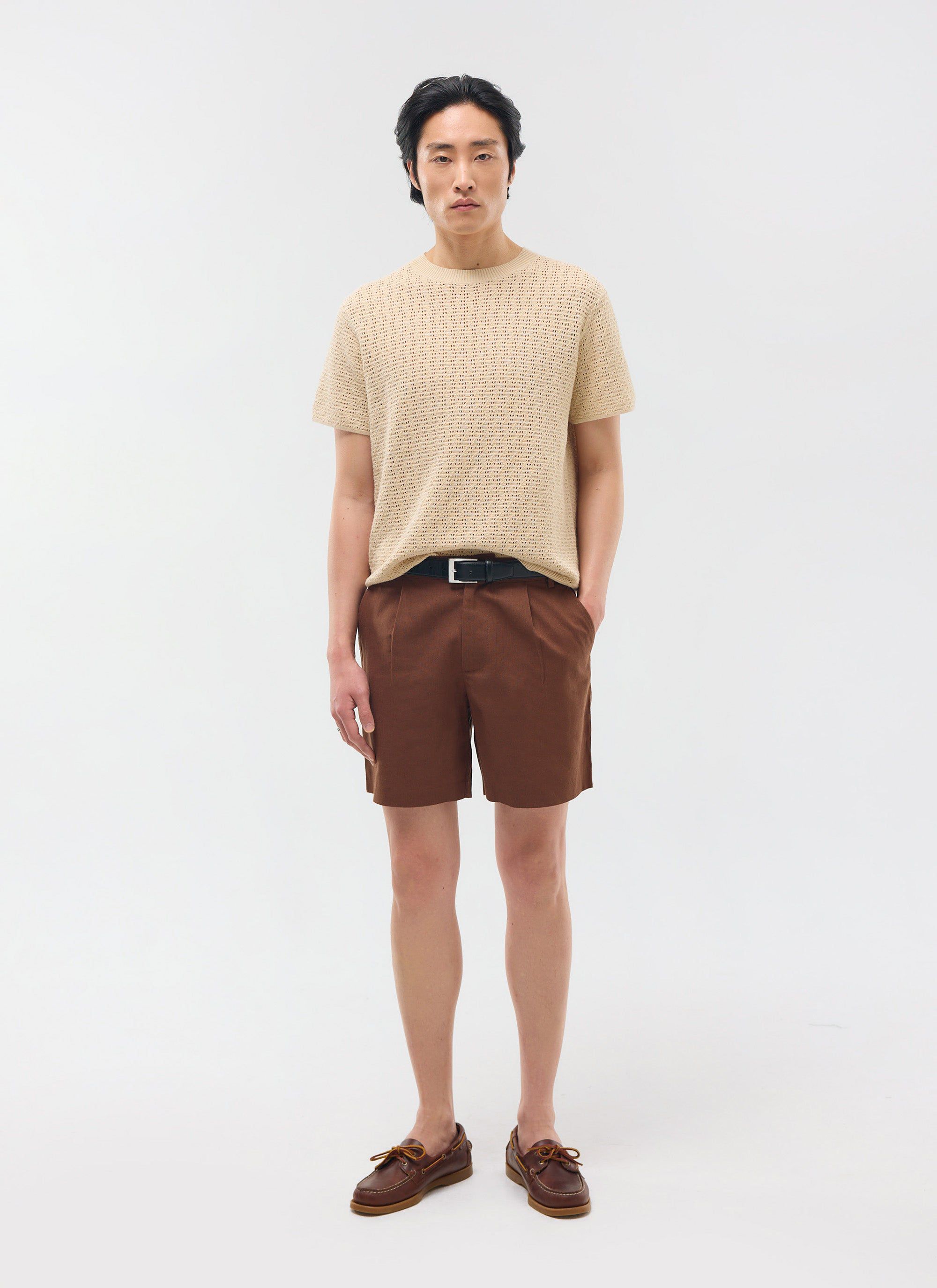 The Percival Pleated Linen Shorts in brown, shown full-length on a model styled with a beige knit t-shirt and boat shoes.