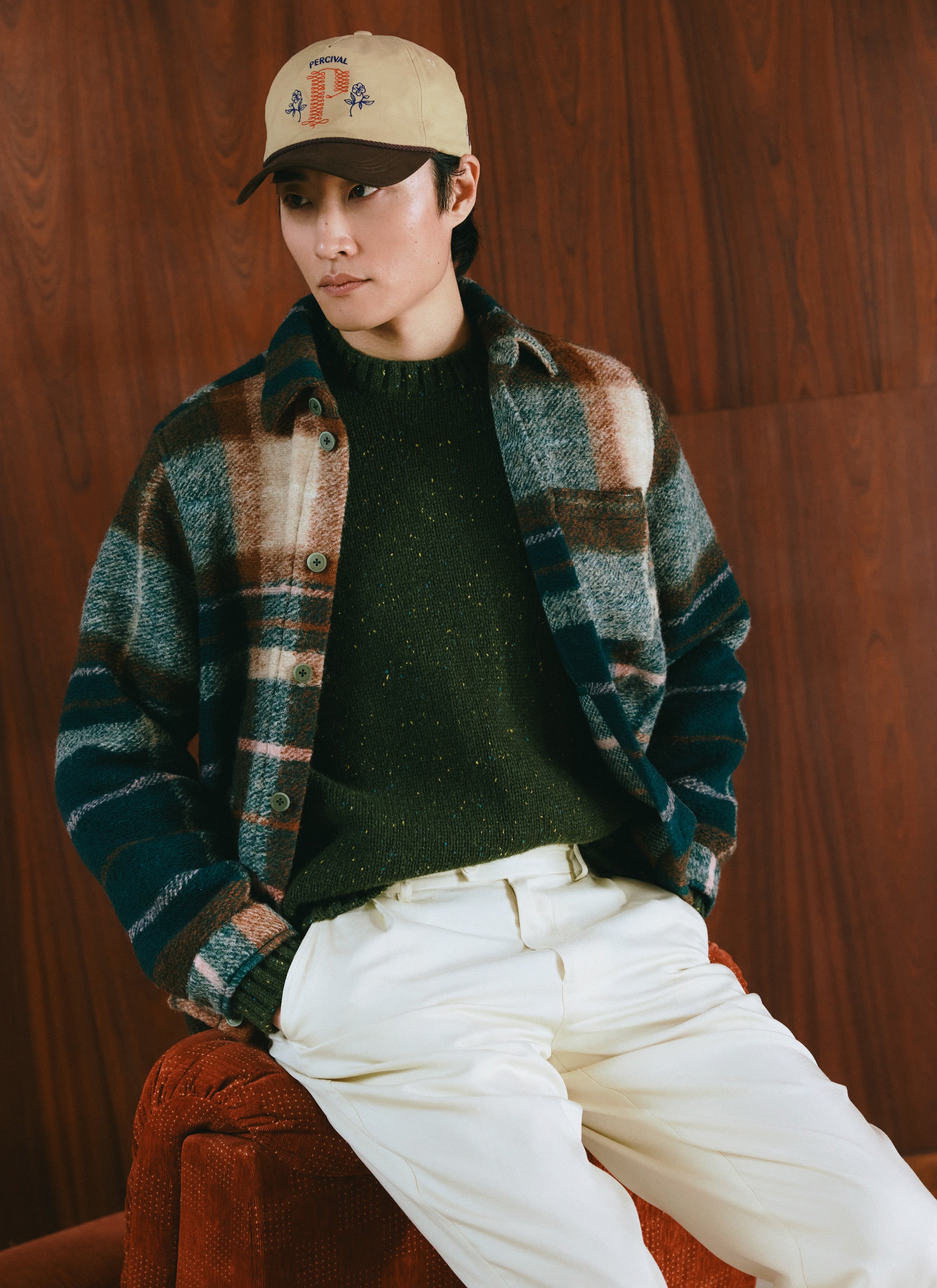 A model wearing the Percival multi check wool Knowles overshirt over a green knit jumper and white trousers.