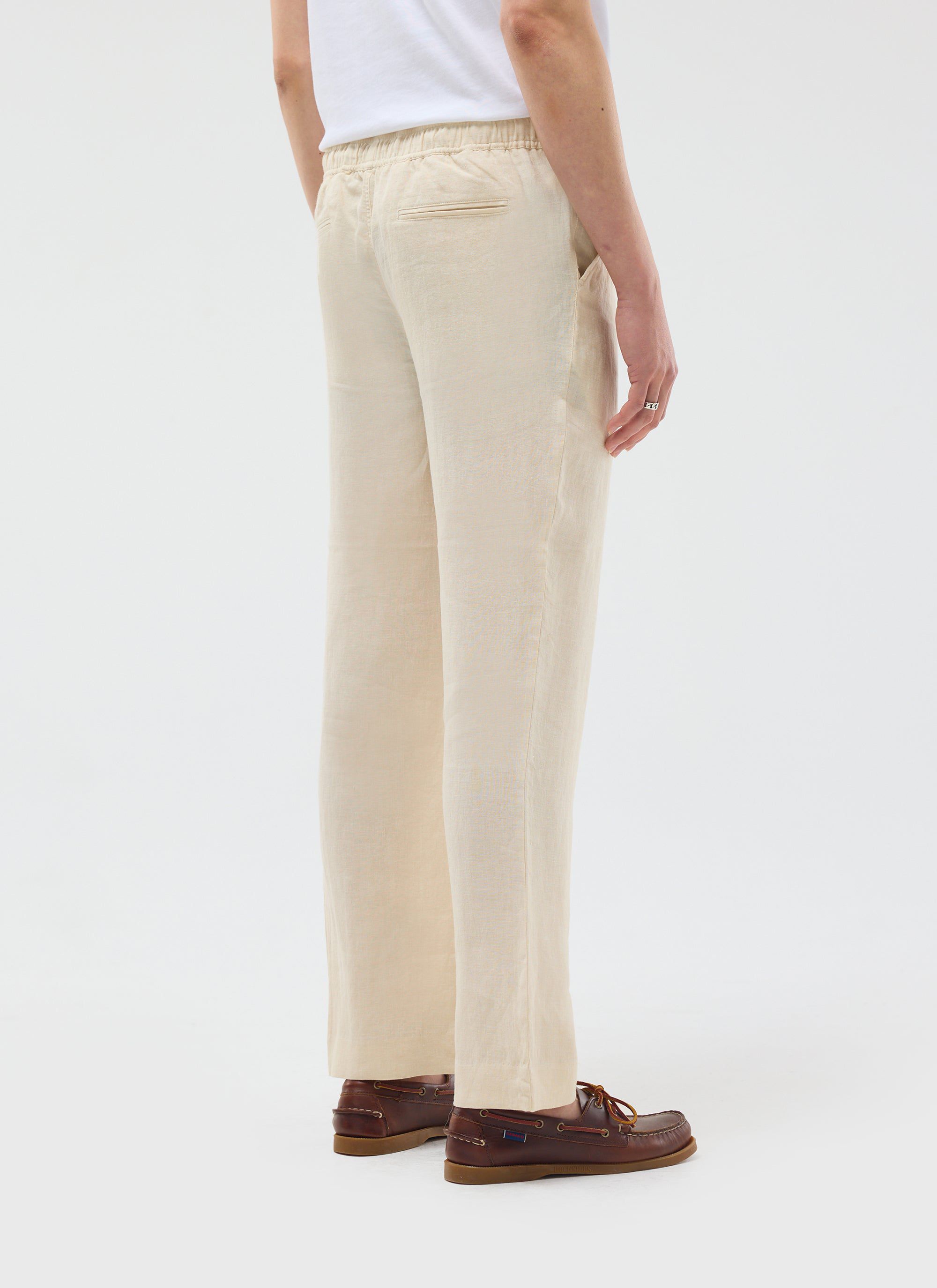 A model, shot from behind, wears the Percival cream Linen Everyday Trousers with brown boat shoes and a white t-shirt.