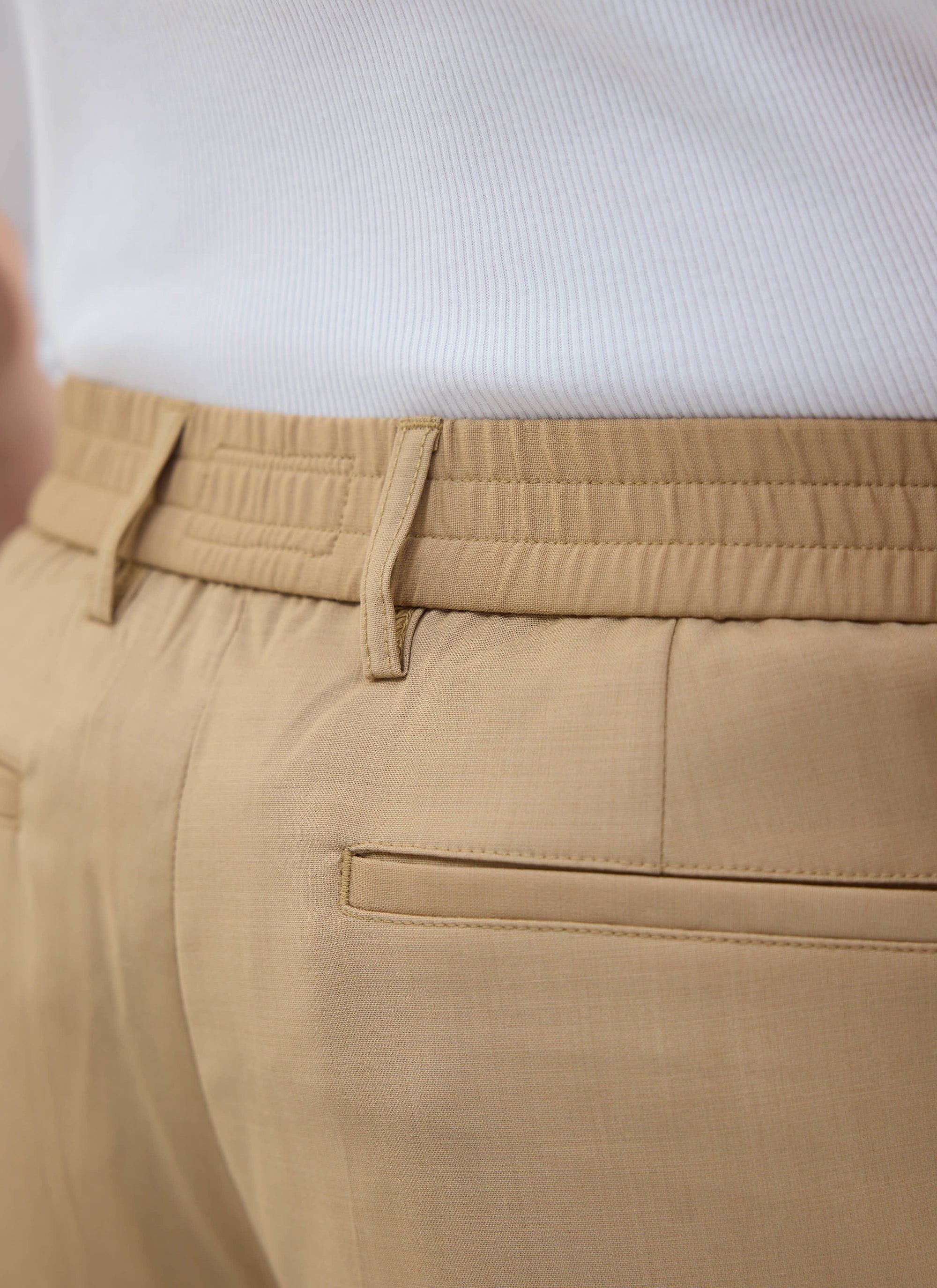 A close-up of the elasticated waistband and back pocket of the tan tailored trousers from Percival.
