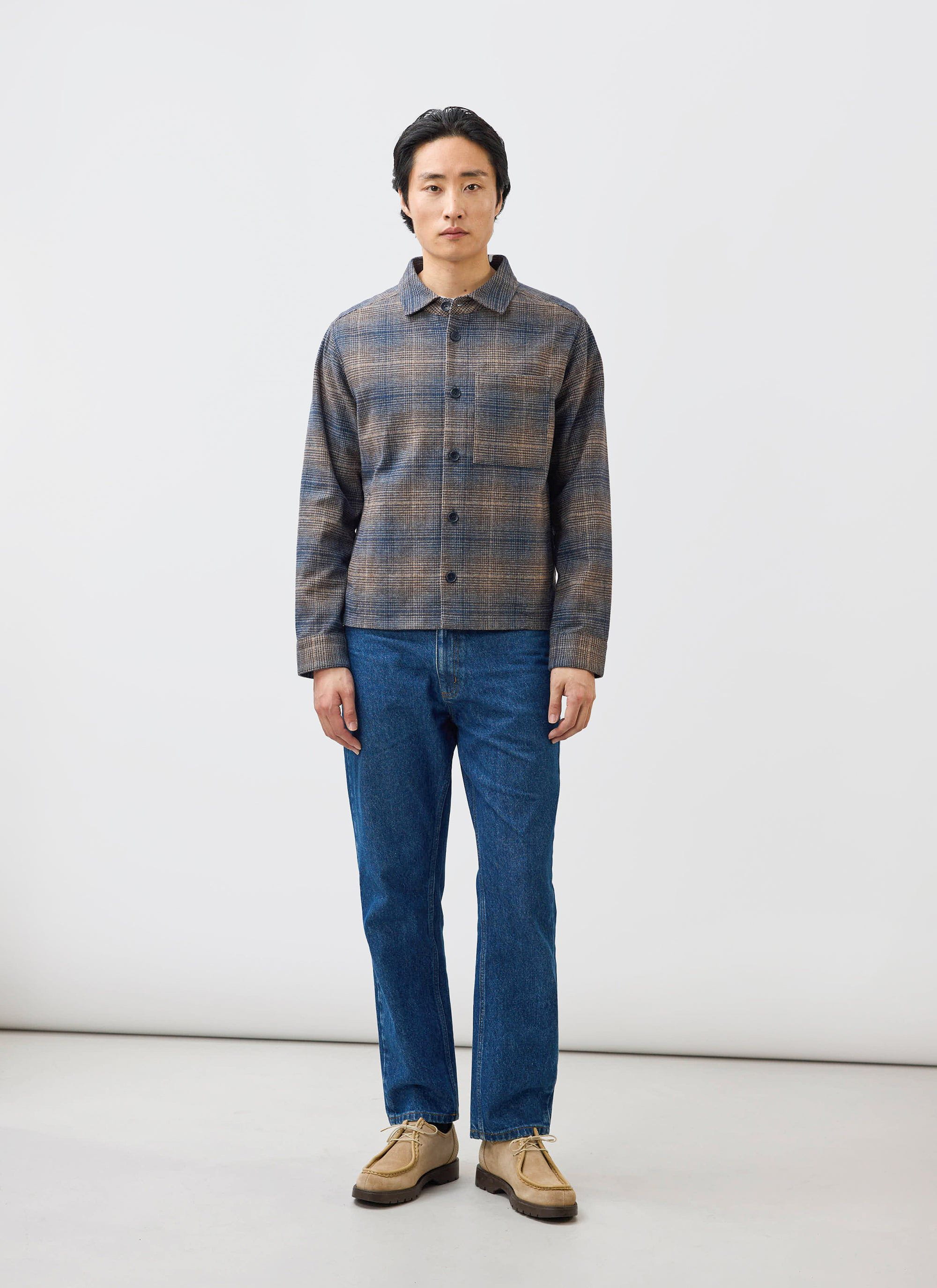 A model wears the Percival Luton Check Overshirt in brown, styled with blue jeans and tan shoes in a studio setting.