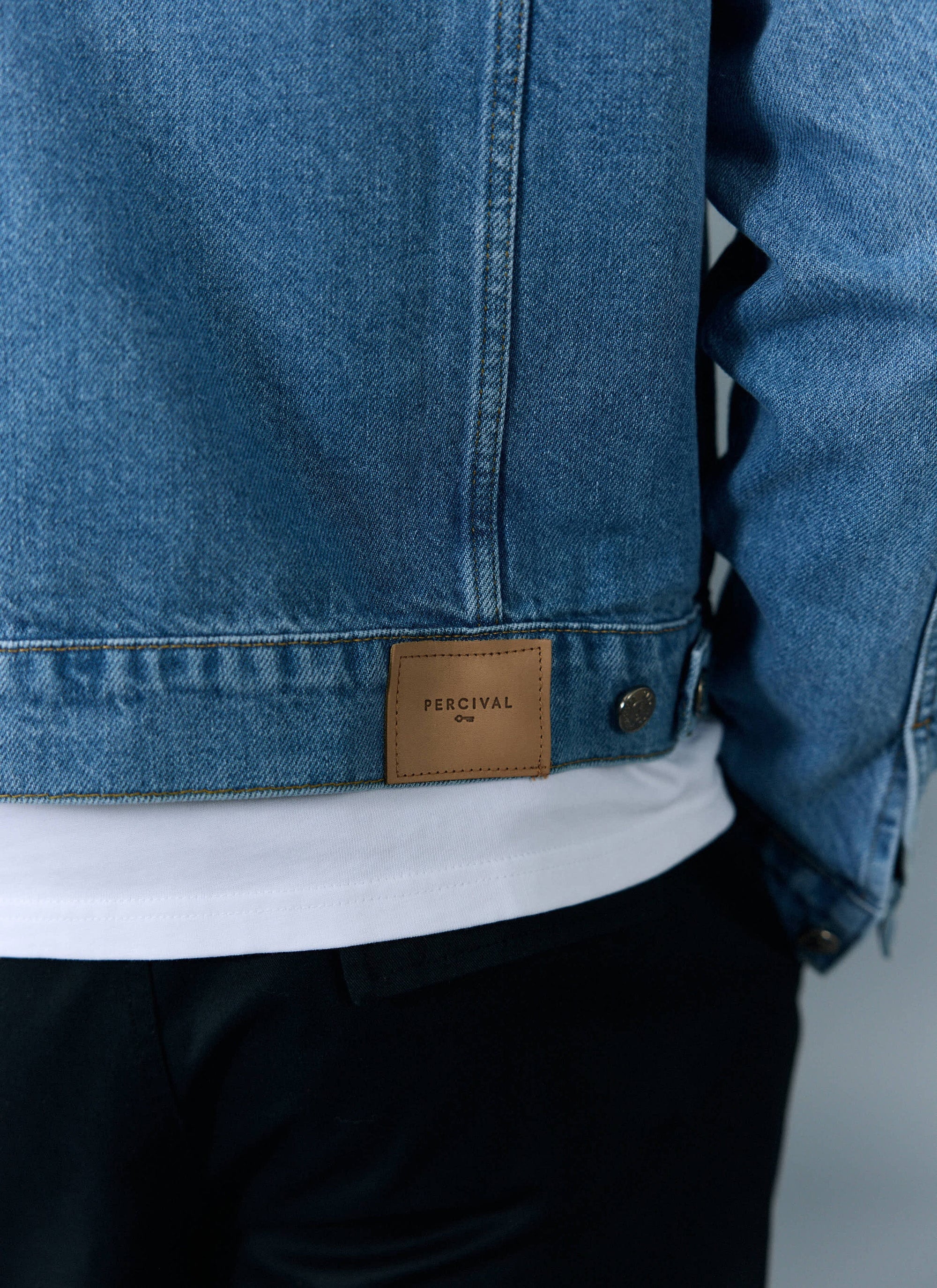 A close-up of the back of the Percival Western Trucker Jacket in light wash blue denim, showing the brown leather patch.