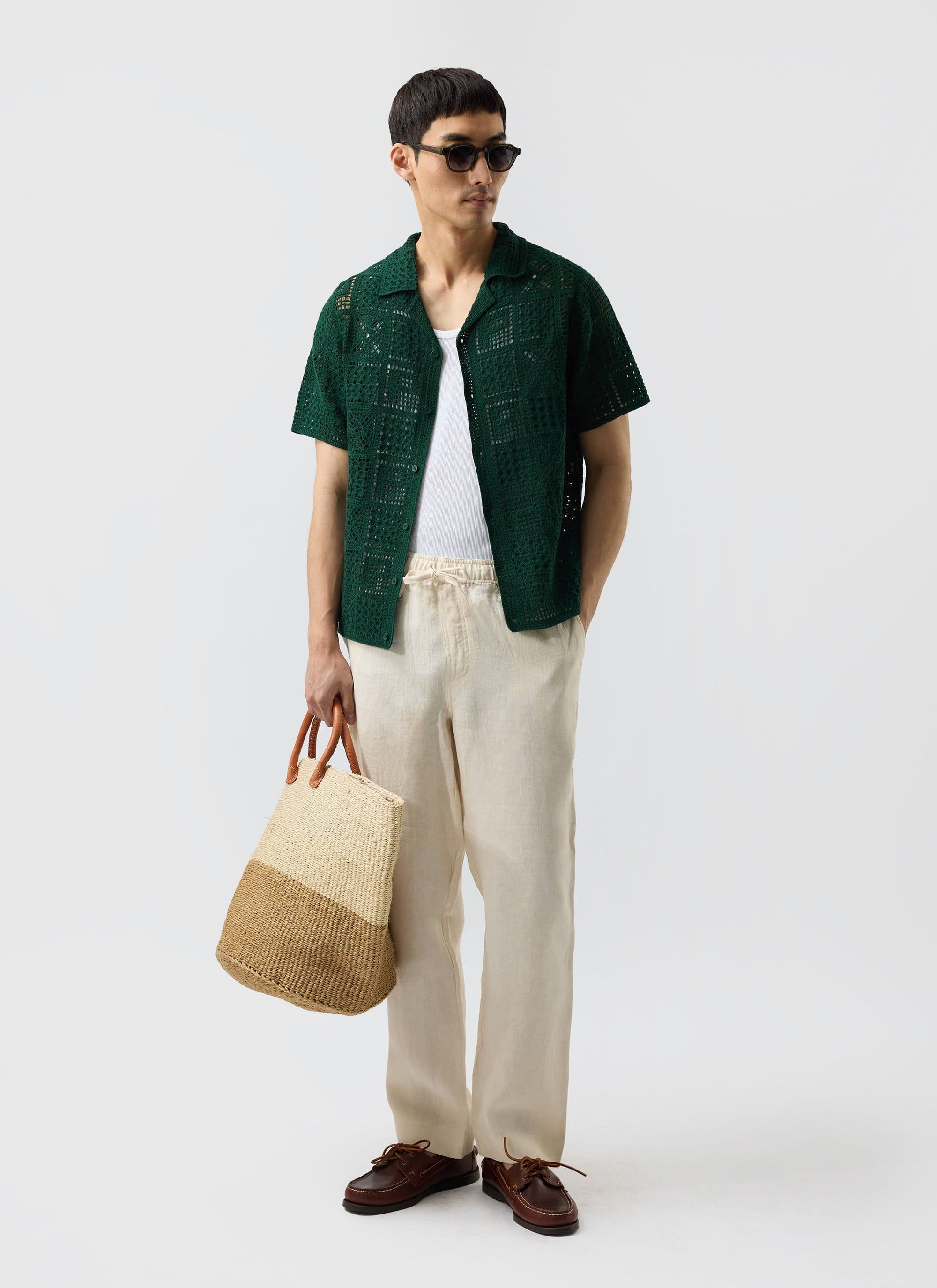 A model wears the Percival Crochet Groundsman Shirt in forest green over a white vest with ecru trousers and sunglasses.