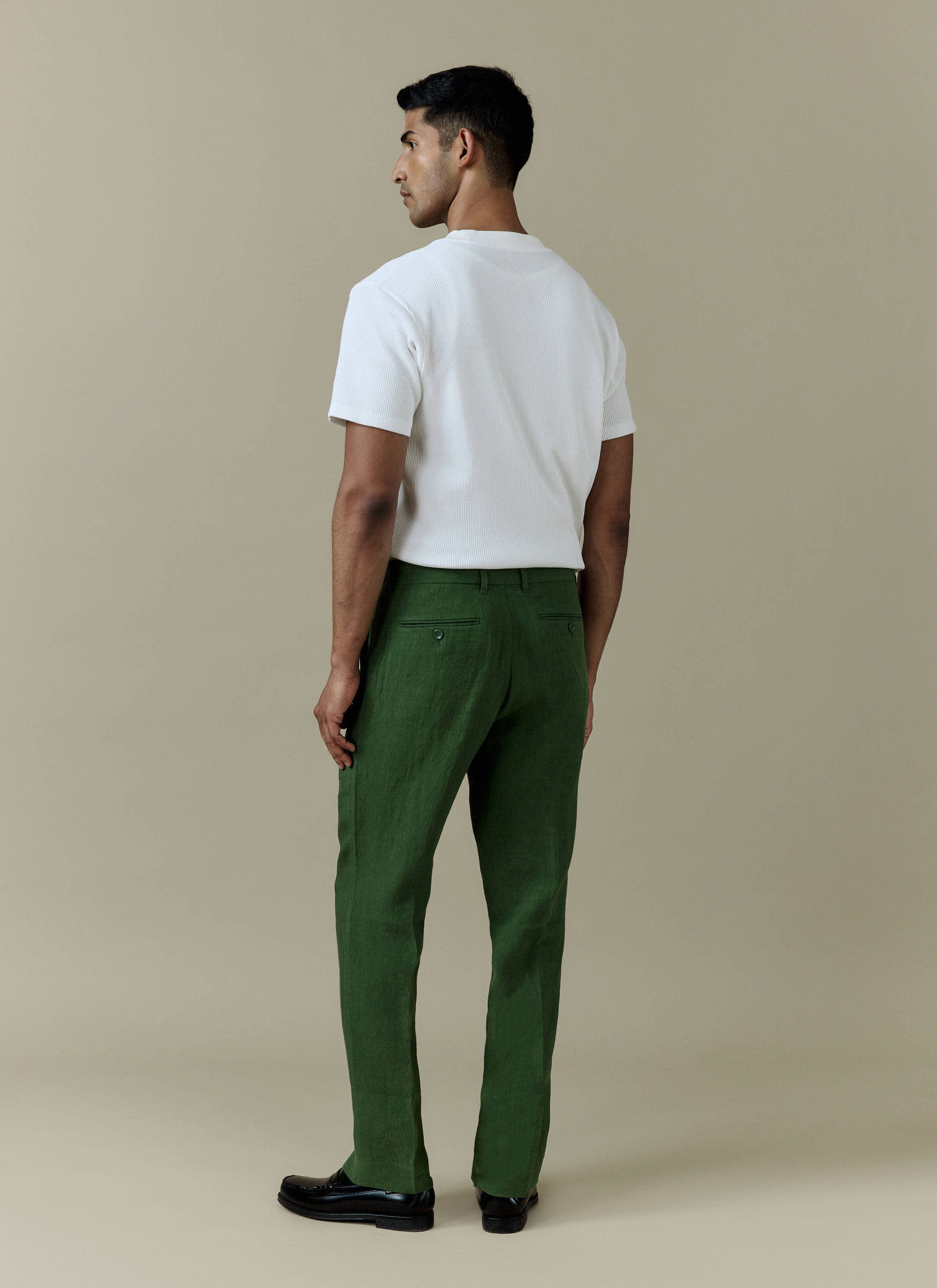 Rear view of the forest green Percival Tailored Linen Trousers, styled with a white t-shirt and black loafers.