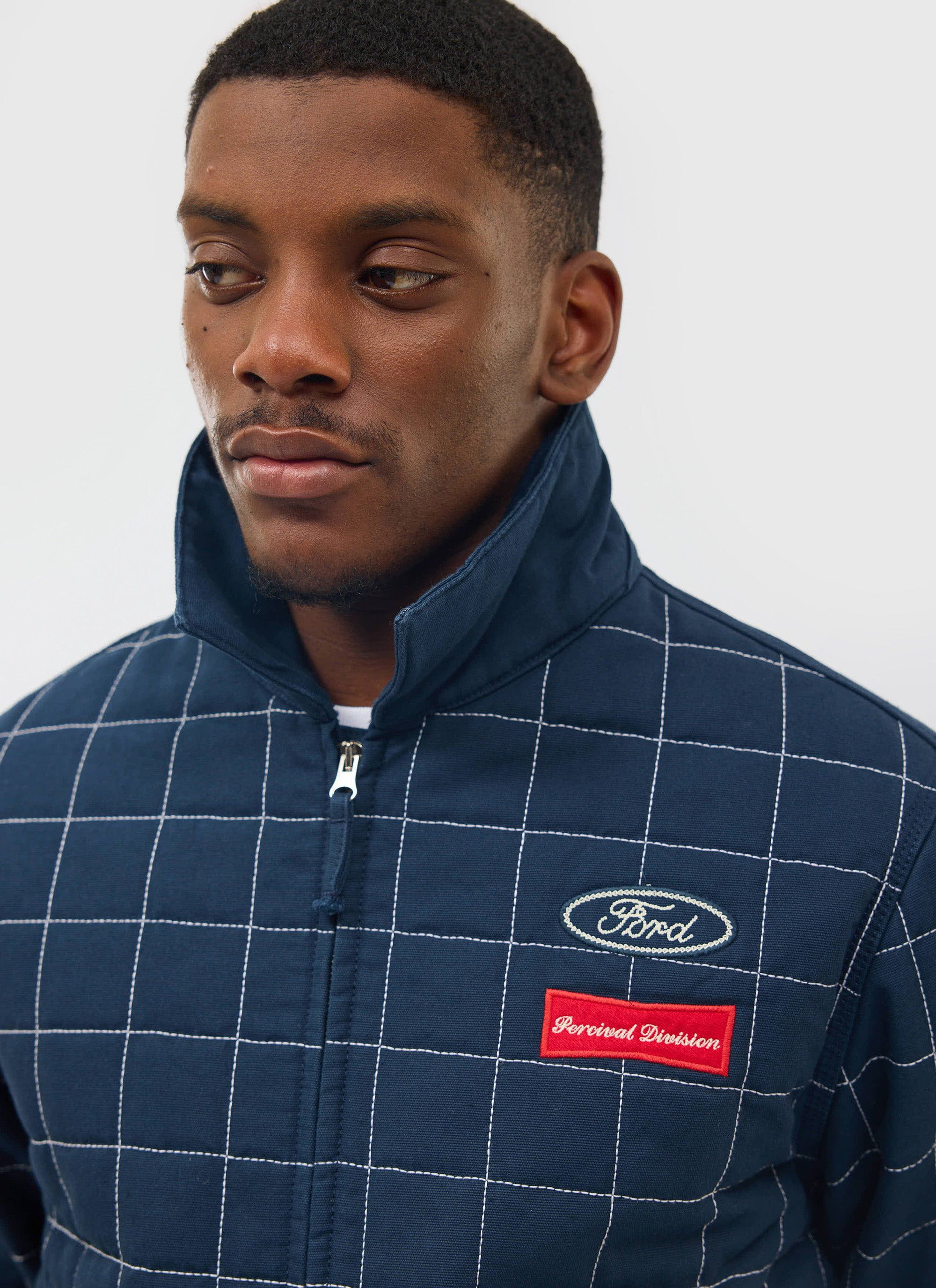 Close-up of a man wearing the navy quilted Percival x Ford Garage Harrington jacket, showing the embroidered logos.