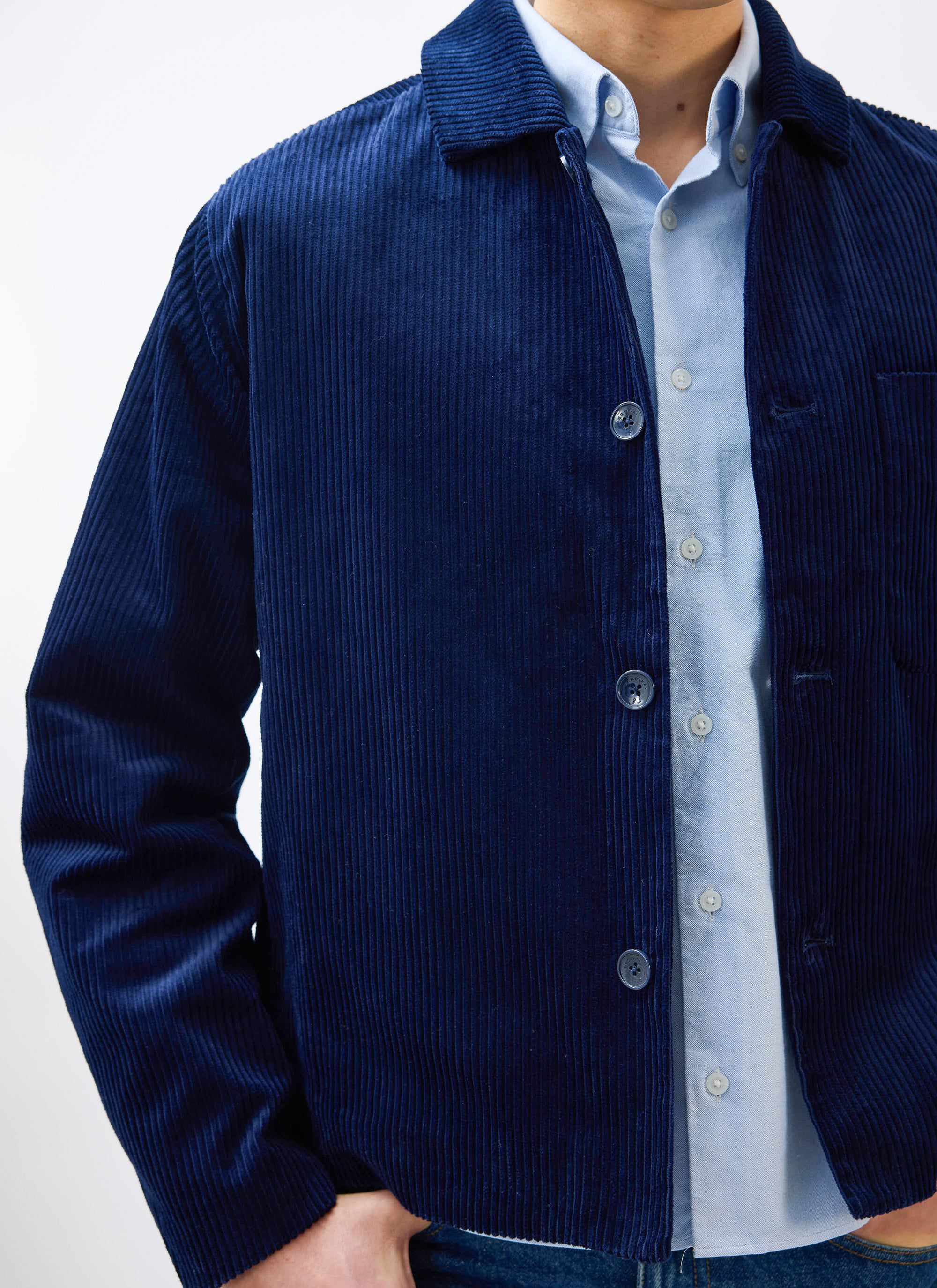 A close-up of a model wearing the navy blue Percival Cord Overshirt layered over a light blue button-down shirt.