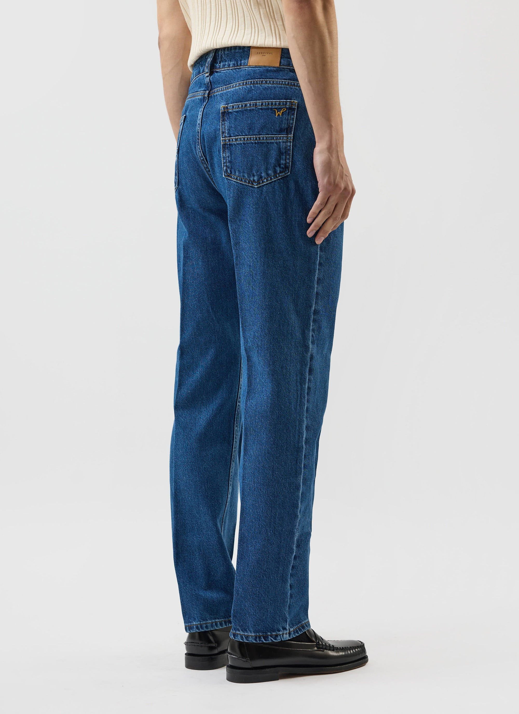 A back view of a model wearing the Percival x Warren Stay Press Denim Jeans in a mid-wash blue, showing the pocket detail.