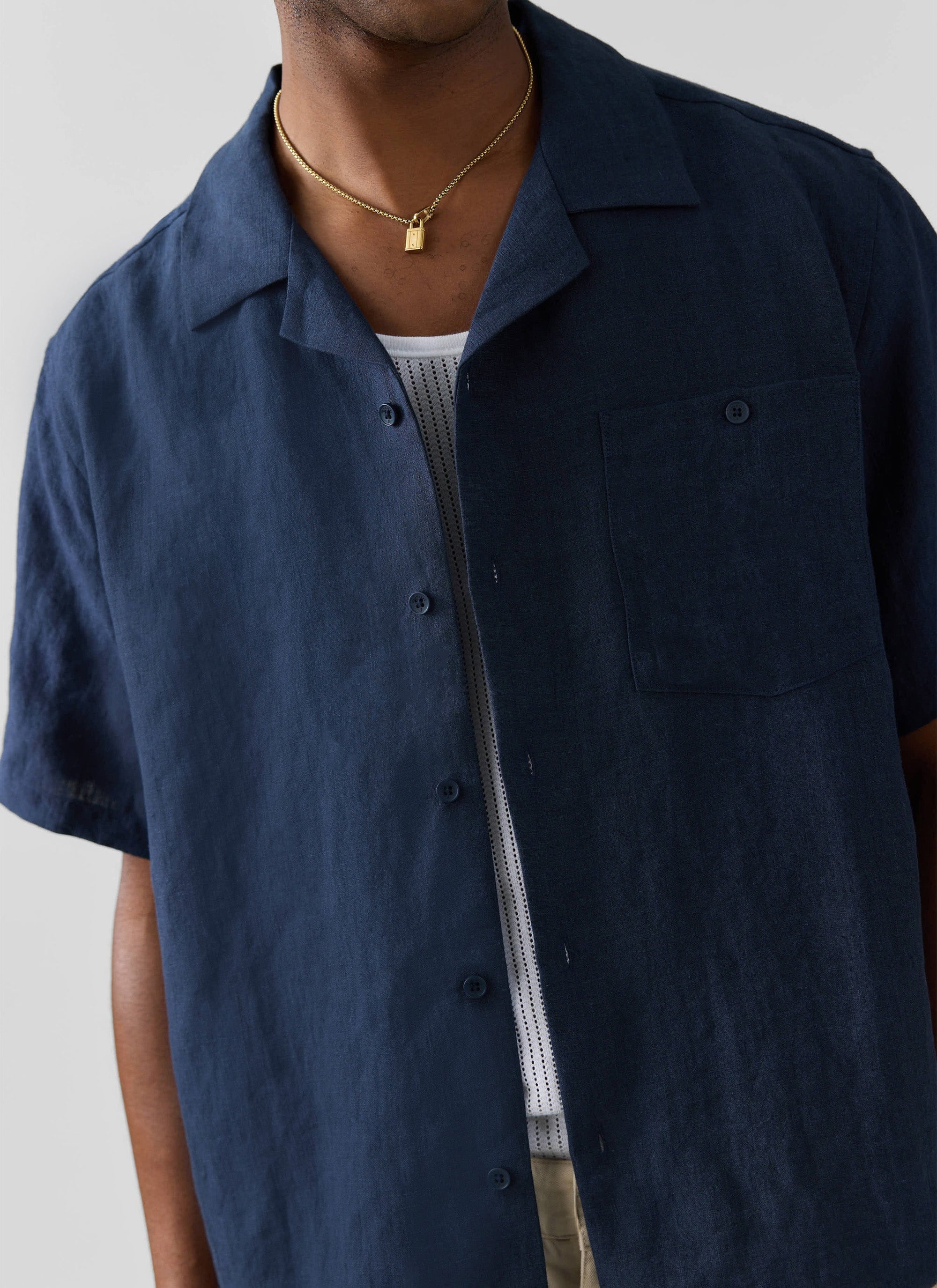 Close up of a model wearing the navy linen short sleeve cuban shirt from Percival, styled open over a white vest.