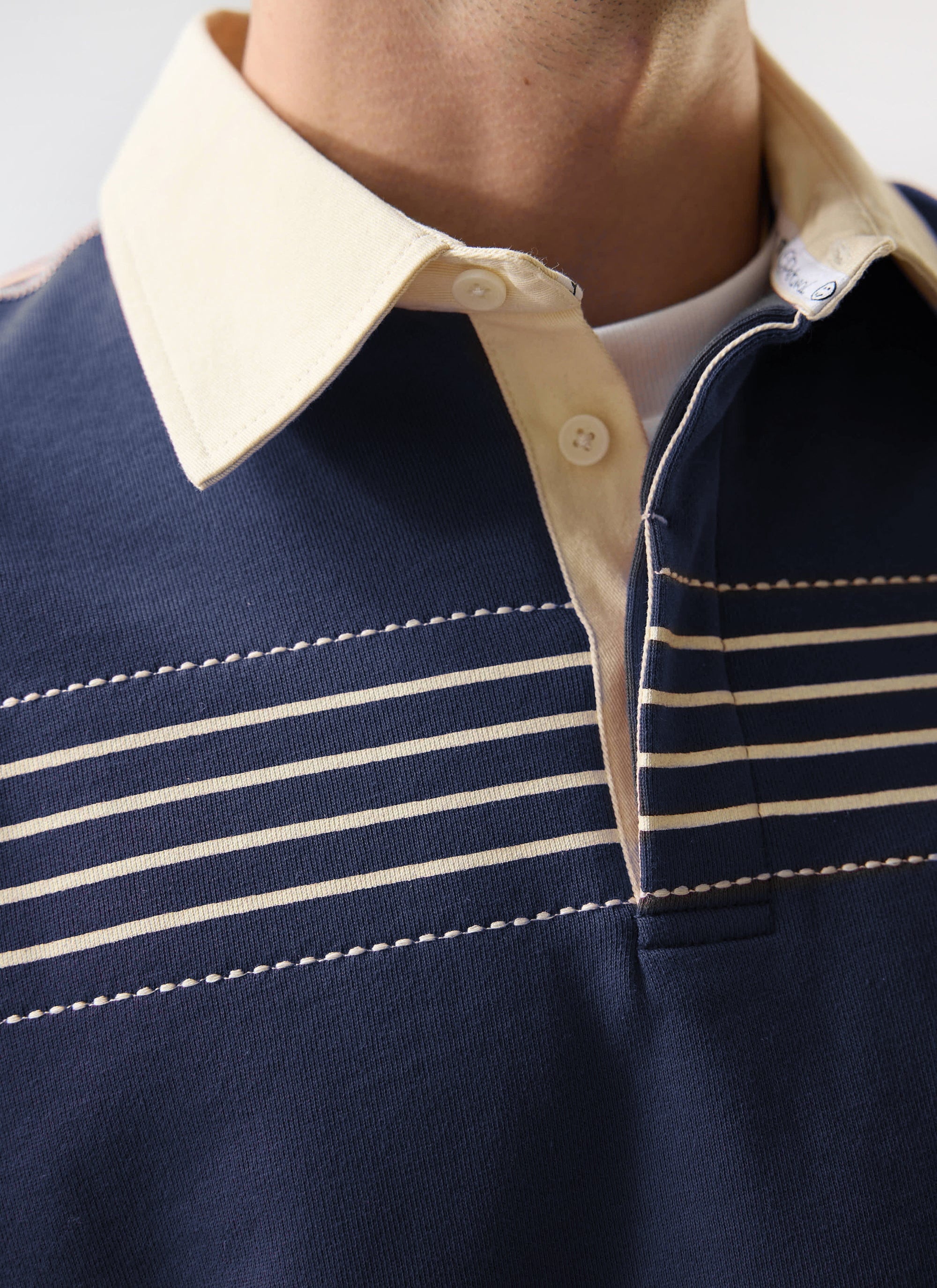 A close-up of the Percival Editor Striped Rugby Polo in navy, highlighting its cream contrast collar and stitch detail.