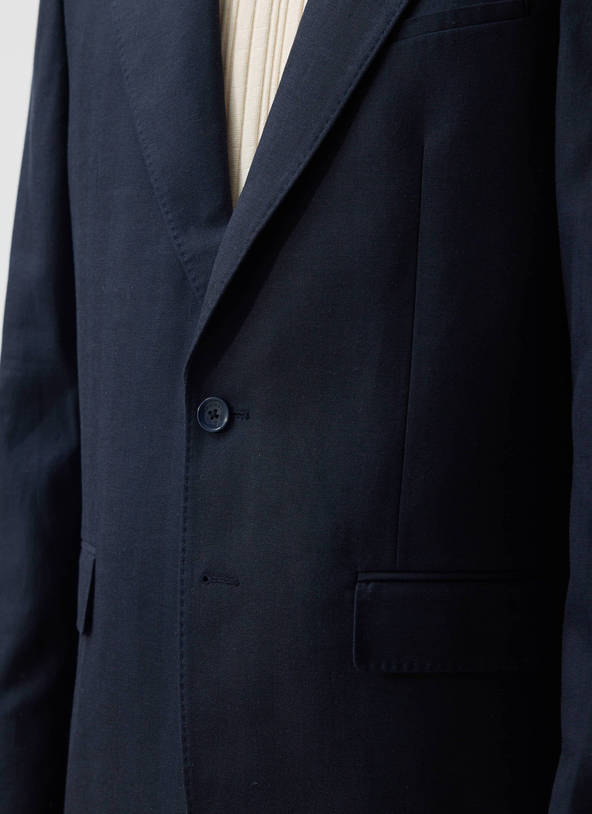 A close-up of the Percival Lyocell Tailored Blazer in navy, showing the lapel, pocket detail, and branded button.