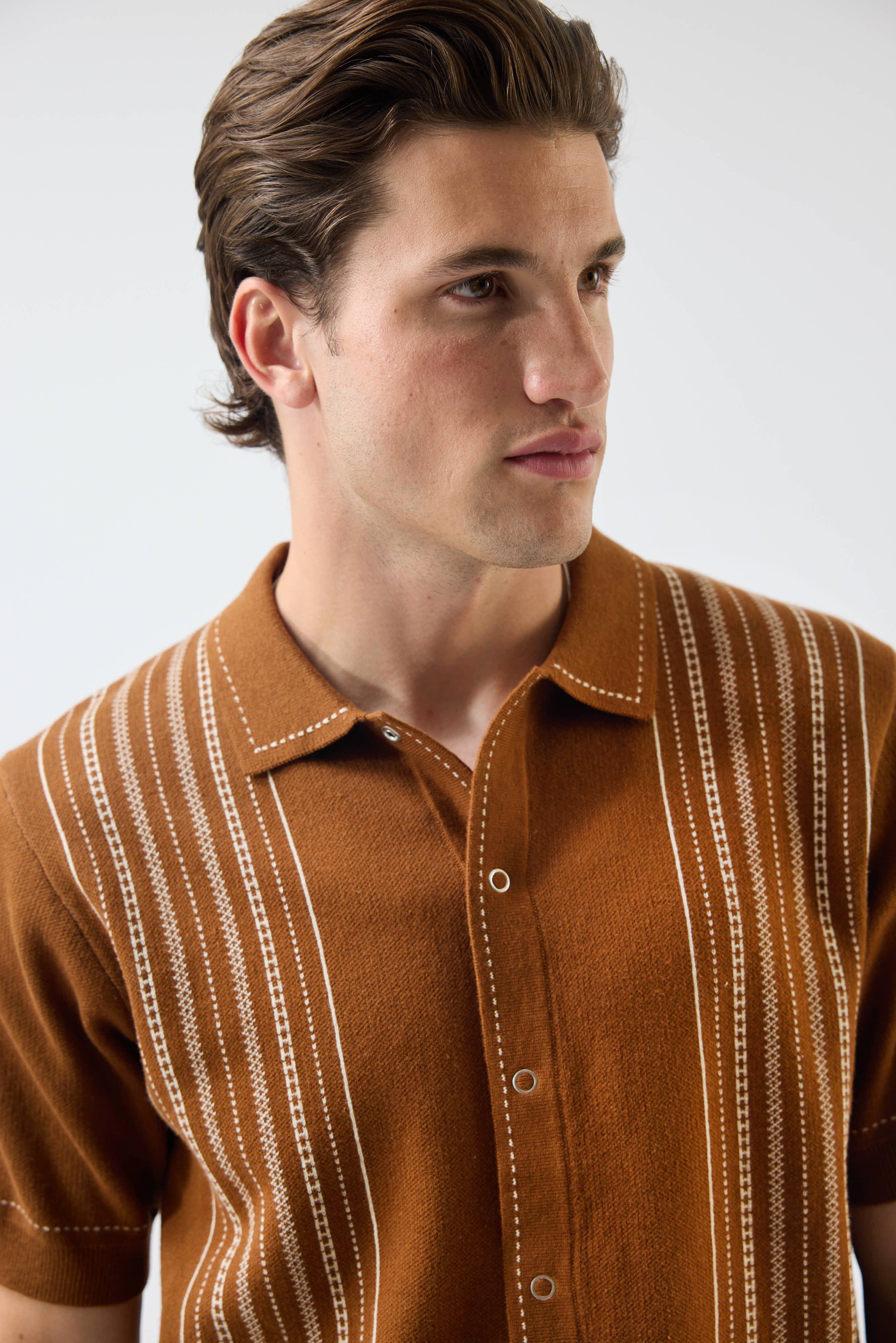 A close-up shot of a model in the Percival Accolades Knitted Shirt in tobacco brown, showing the book spine jacquard detail.