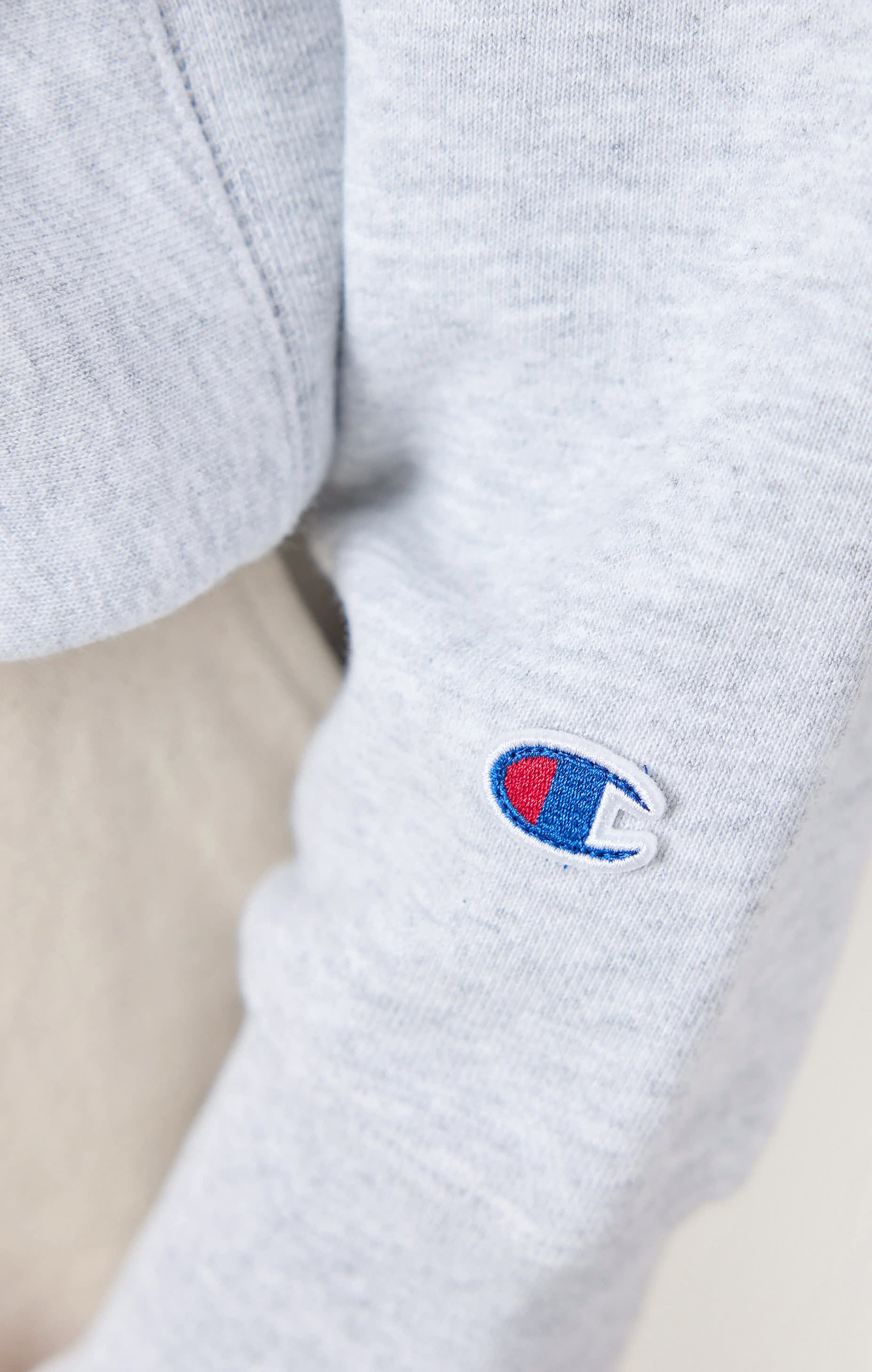 A close-up of the embroidered Champion logo on the sleeve of the grey jersey sweatshirt from the Percival collaboration.