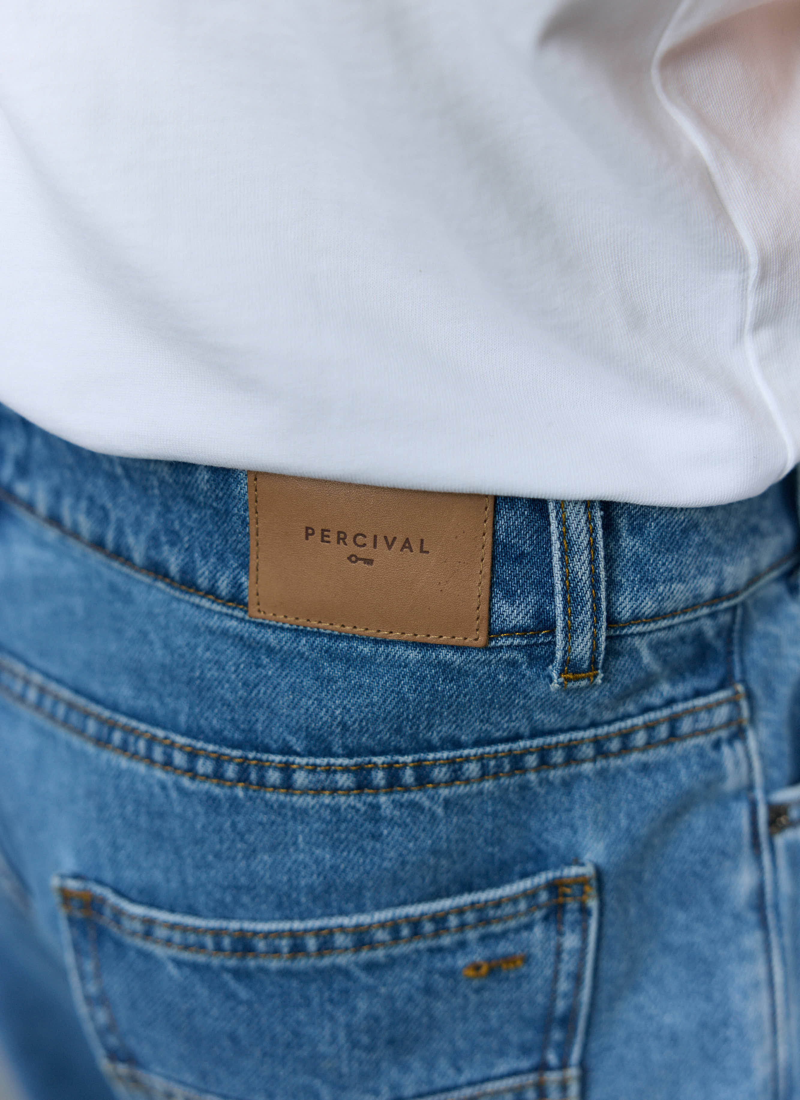 A close-up of the back of the Percival Wide Leg Denim Jeans in light wash blue, showing the brown leather logo patch.