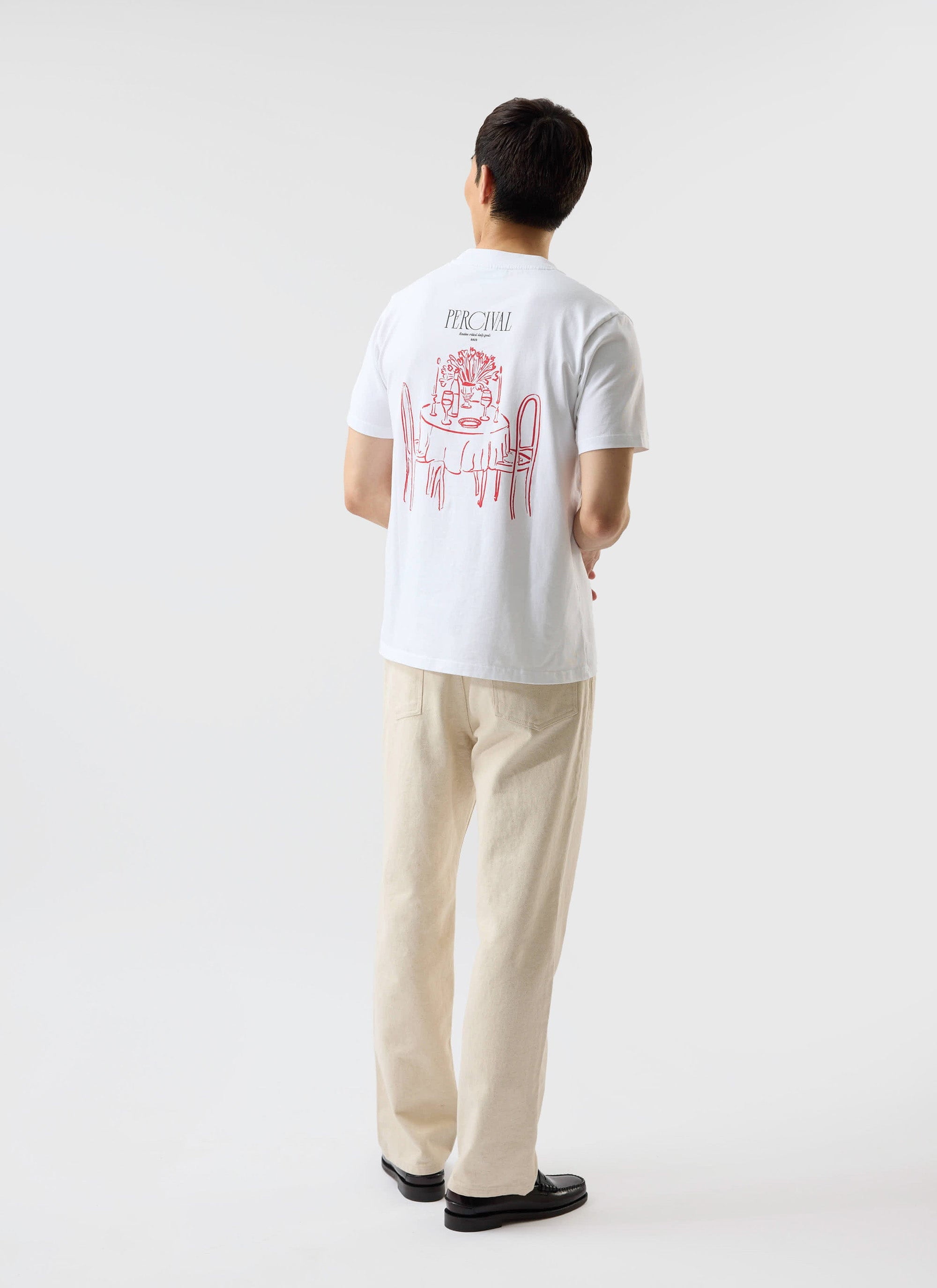 A model seen from behind wears the white Percival Bistro T-shirt, showing the red embroidered graphic on the back.