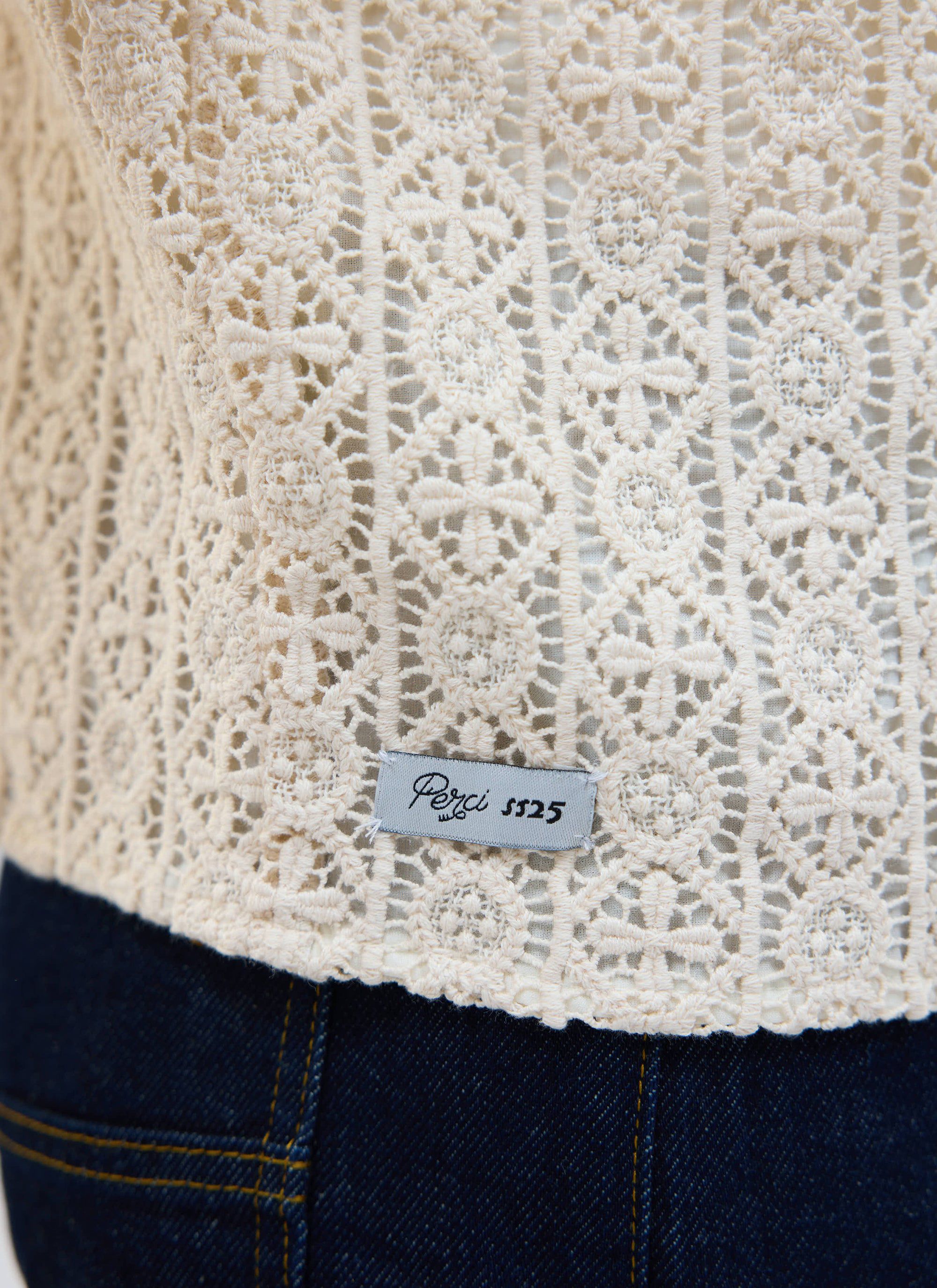A close-up of the intricate crochet pattern and SS25 label on the ecru Elio Cuban Shirt by Percival.
