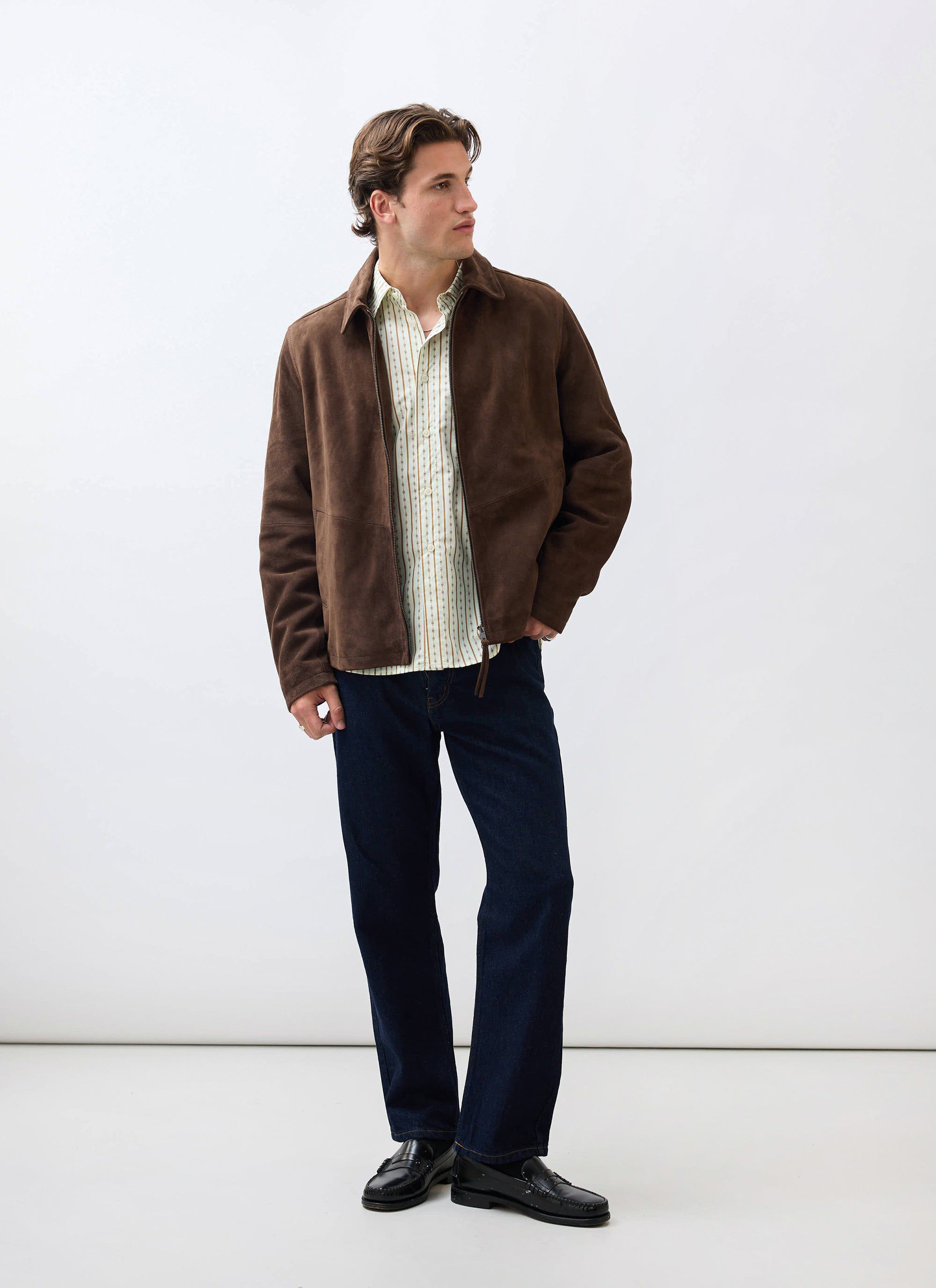 A man models the espresso brown Prologue Soft Suede Jacket from Percival, styled with a patterned shirt and dark jeans.
