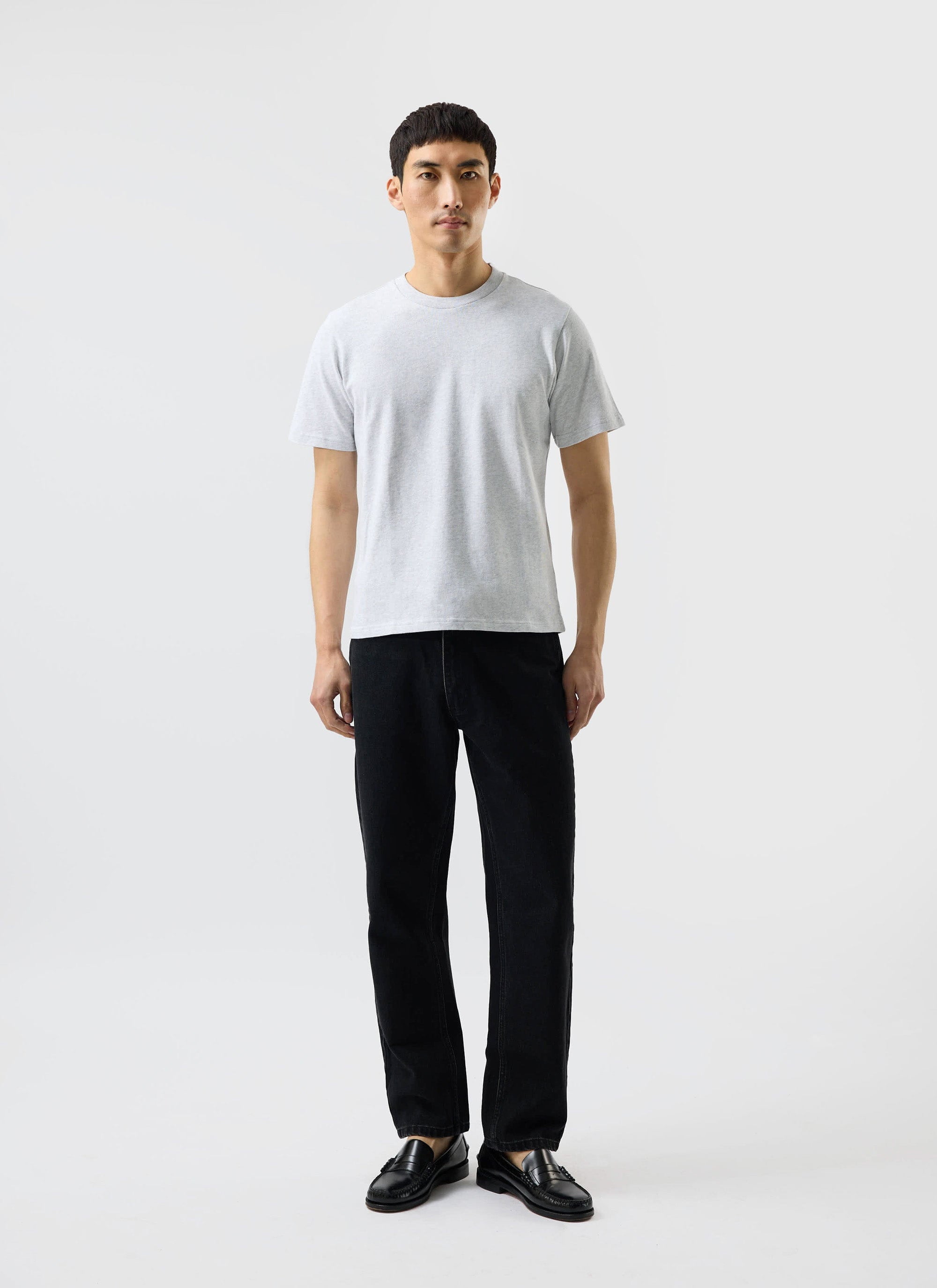 A man models the Percival Cropped Regular Fit T Shirt in grey, styled with black trousers and loafers.